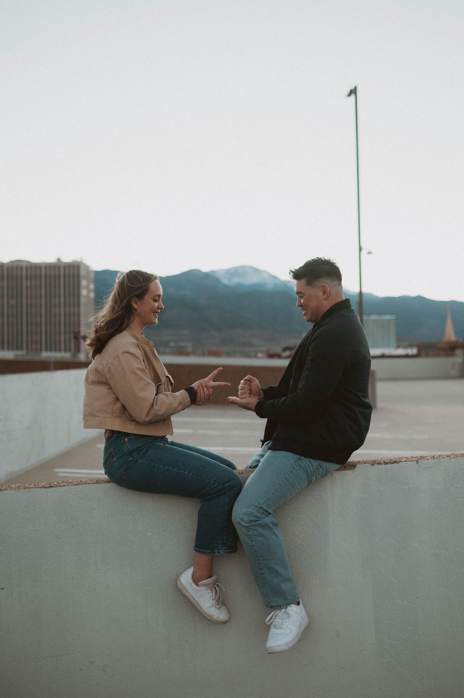 Couple sitting on a rooftop ledge holding hands with mountain cityscape in the background.