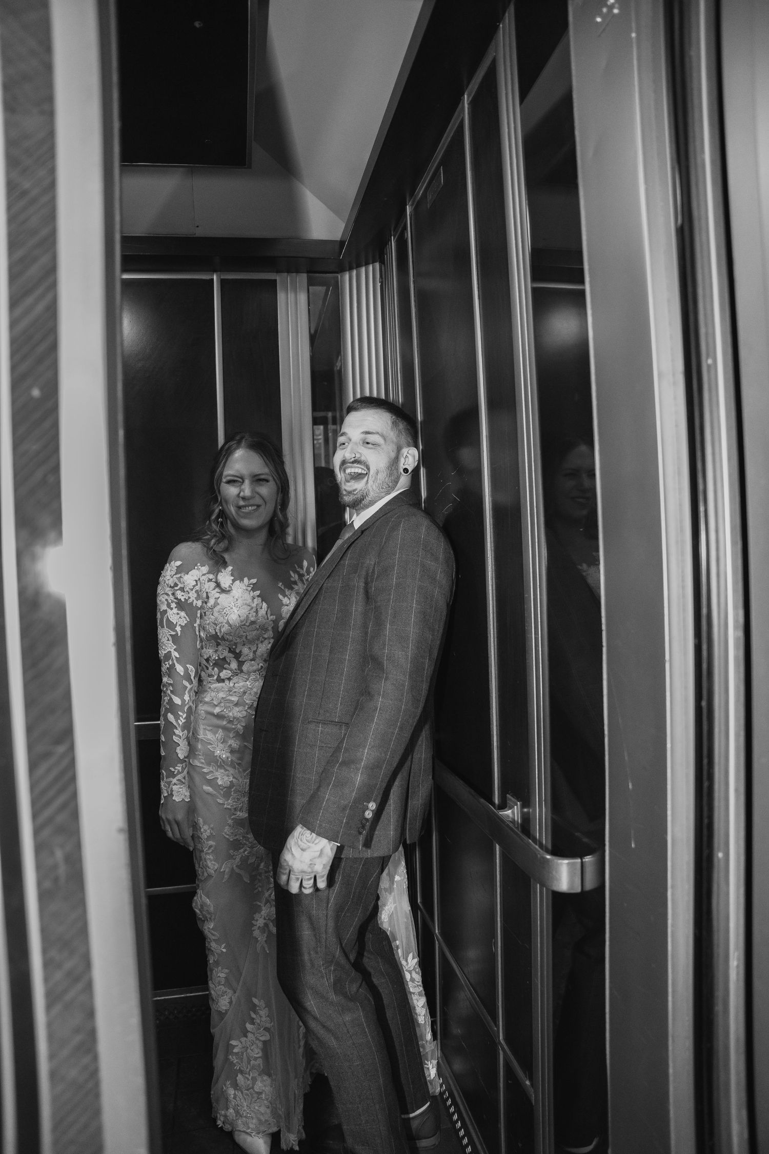 Black and white photo of laughing bride and groom stepping out of an elevator together.