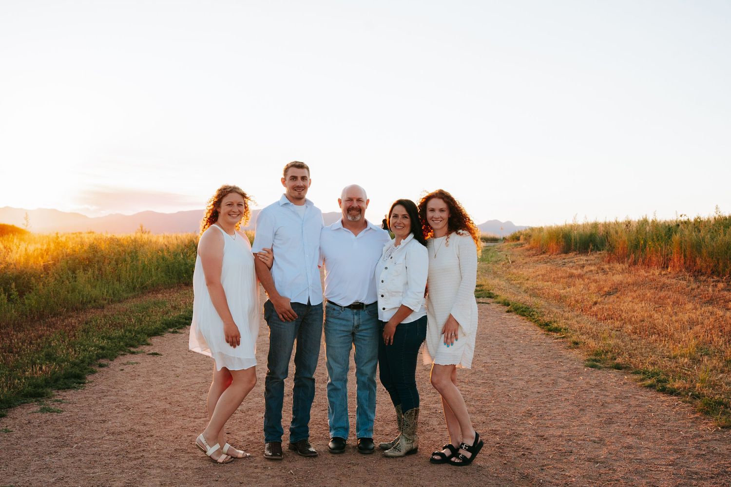Family of five posing on a dirt path at golden hour with mountains in the background.