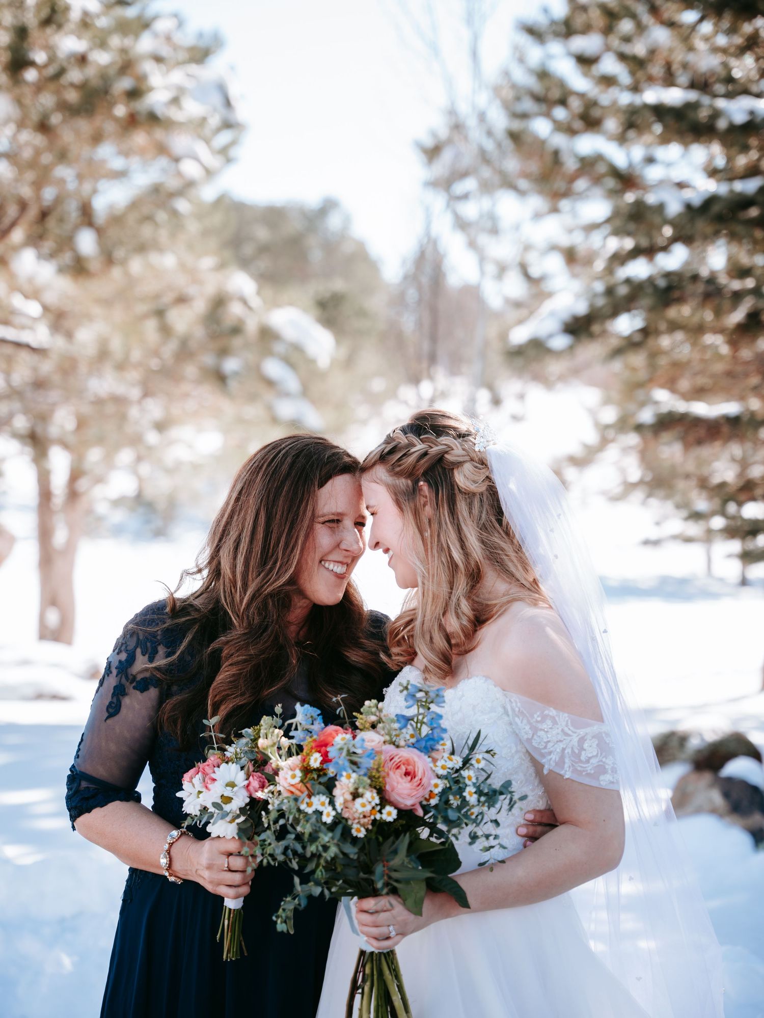 Bride and bridesmaid smiling together in snowy winter wedding outdoor setting.