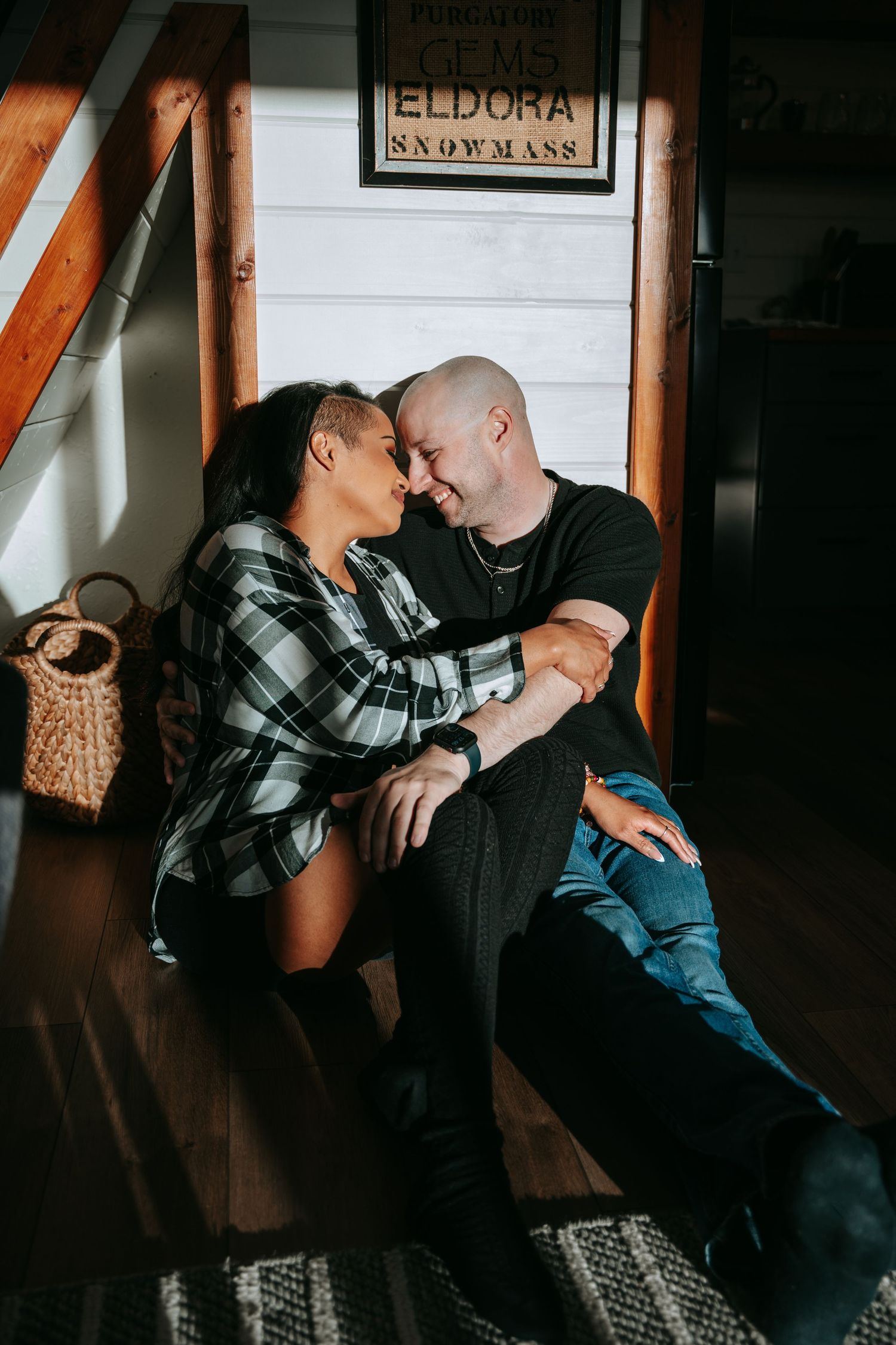 Romantic interracial couple sitting close together on cabin floor, nearly touching foreheads in an intimate moment.
