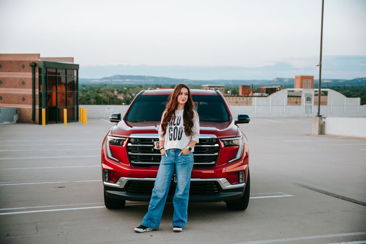 Young woman in jeans posing in front of red truck on rooftop parking lot.