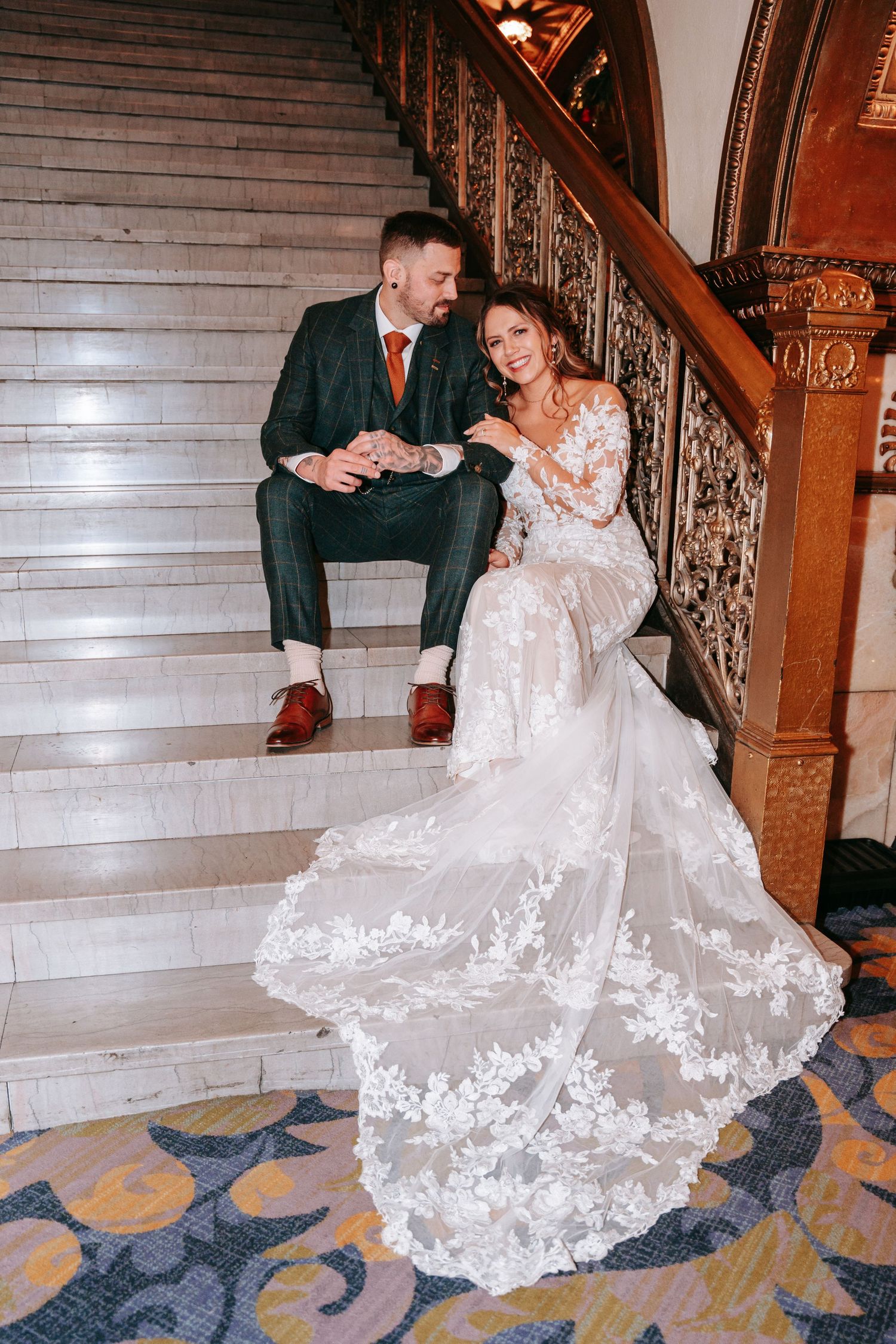 Bride and groom sitting on ornate marble staircase, bride's lace train spread elegantly.