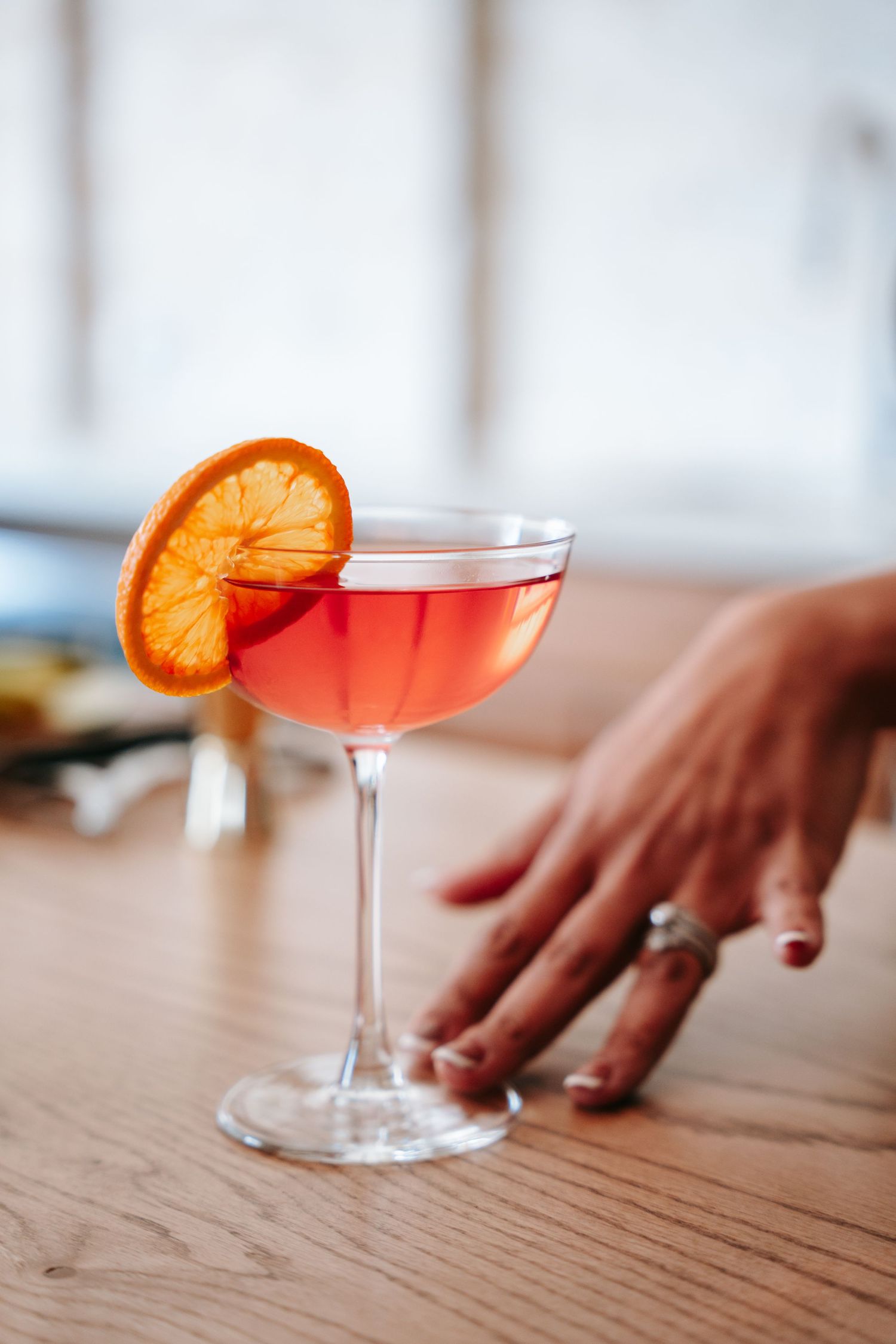 Elegant pink cocktail garnished with dried orange slice in coupe glass on wooden bar.