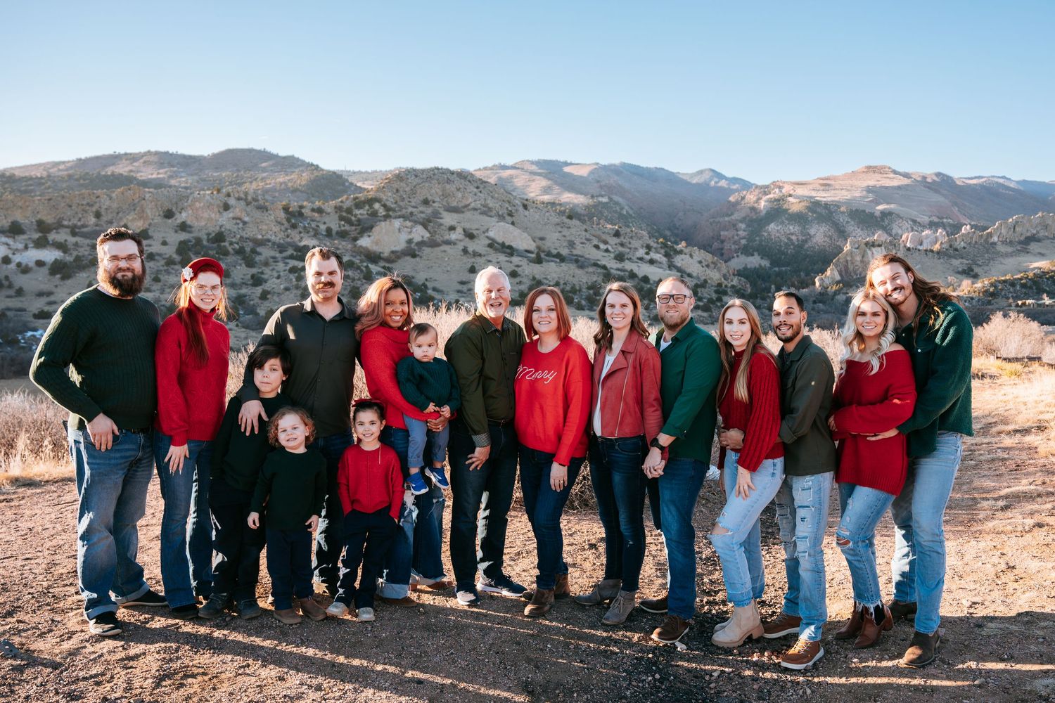 Large extended family group portrait in red and green holiday attire with mountain backdrop.