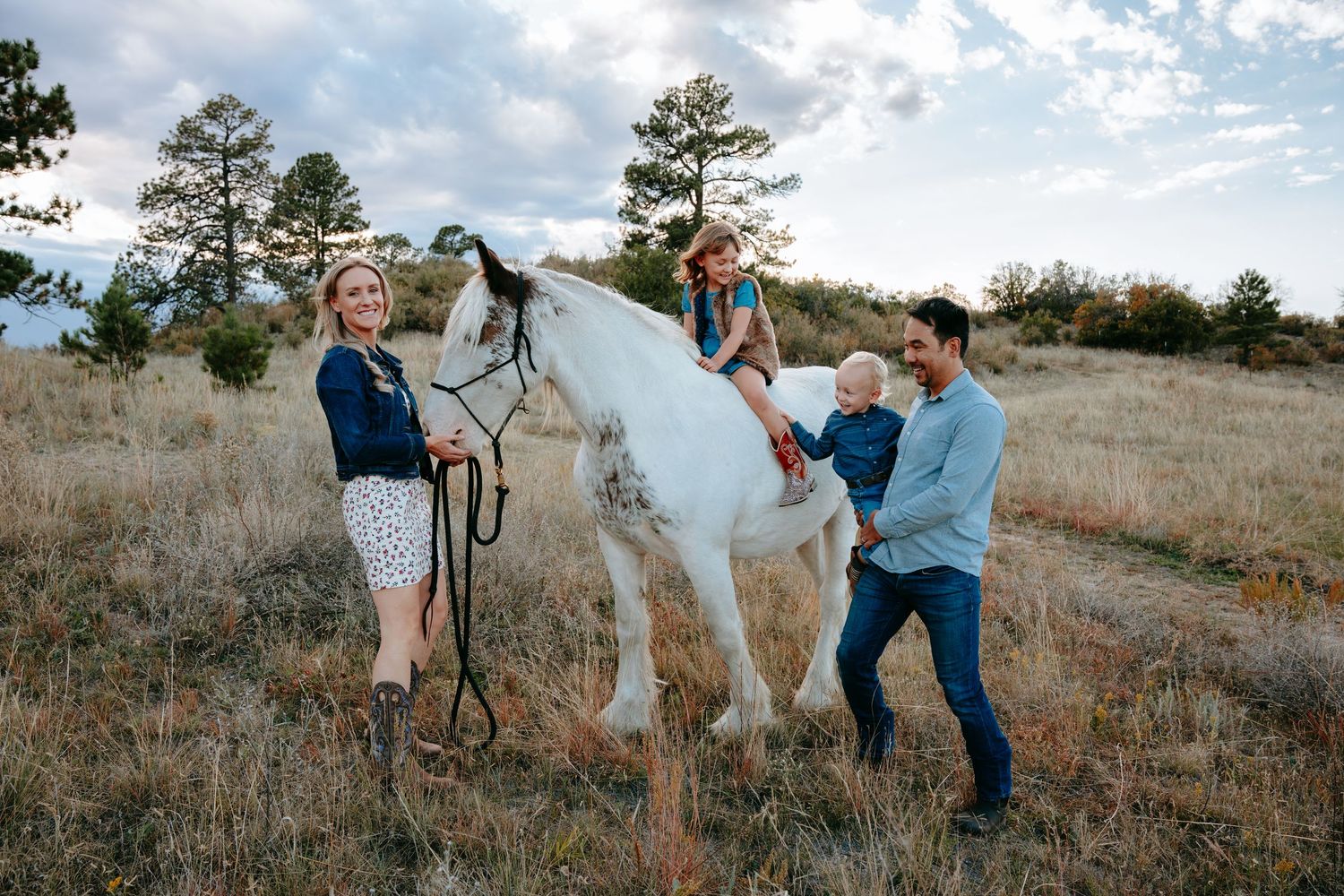 Family with two children and a white horse in a scenic Colorado meadow during fall photo session.
