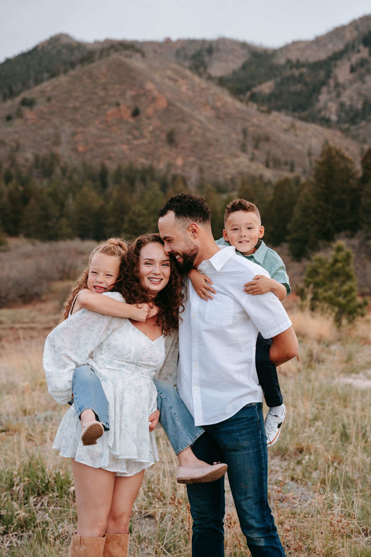Happy family of four embracing outdoors with a mountain landscape in the background.