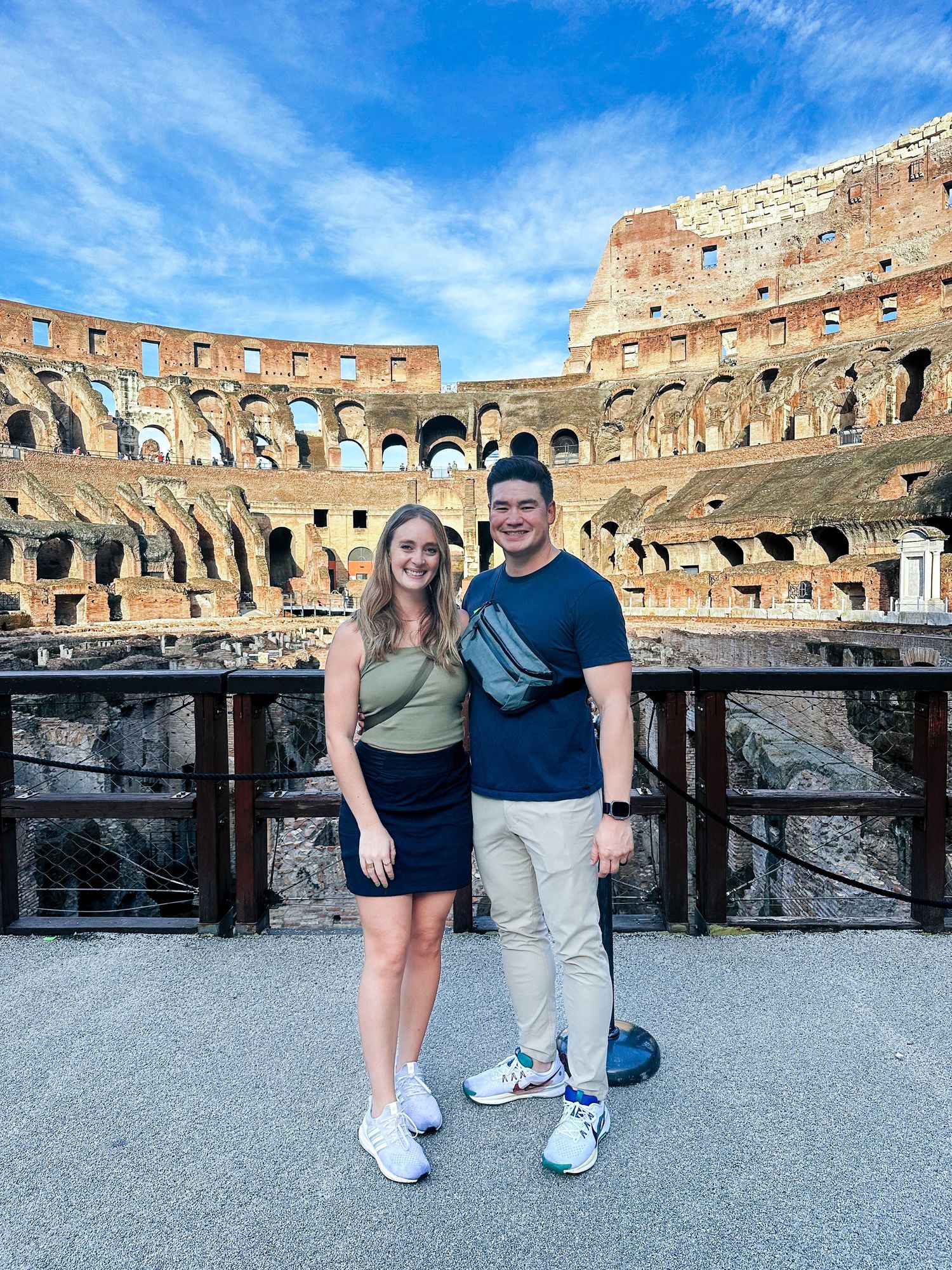 Couple posing together inside the historic Roman Colosseum under a bright blue sky in Rome, Italy.
