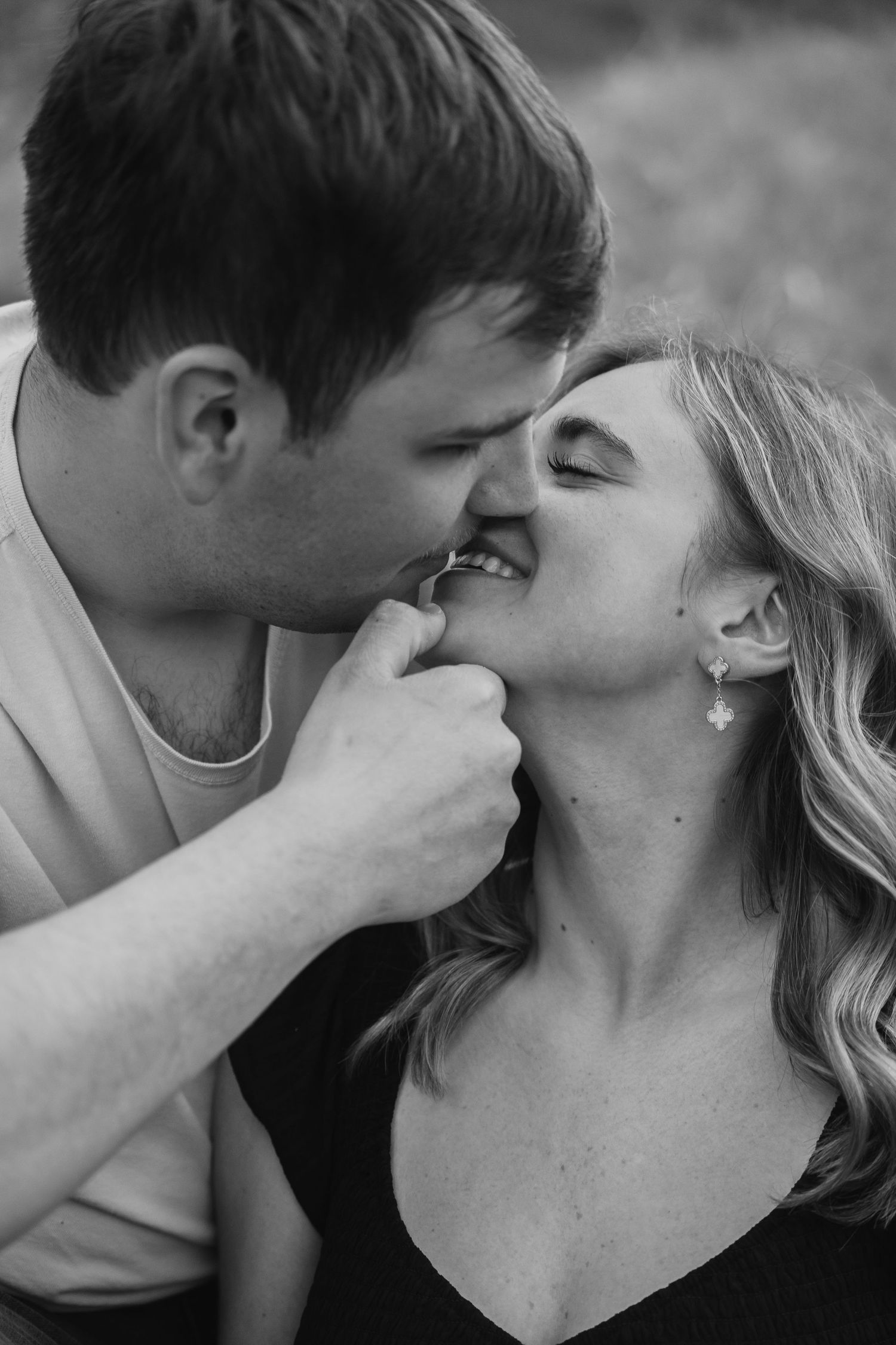 Black and white photo of a couple sharing a tender, playful kiss outdoors during an engagement session.