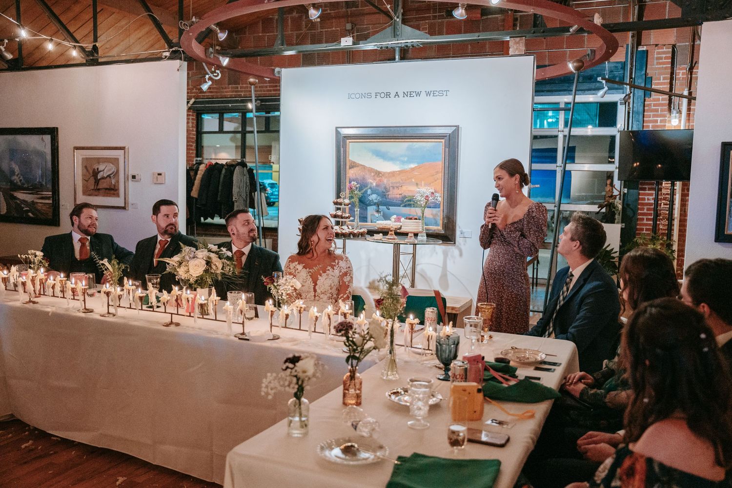 Wedding party seated at a head table adorned with candles and florals during a reception toast.