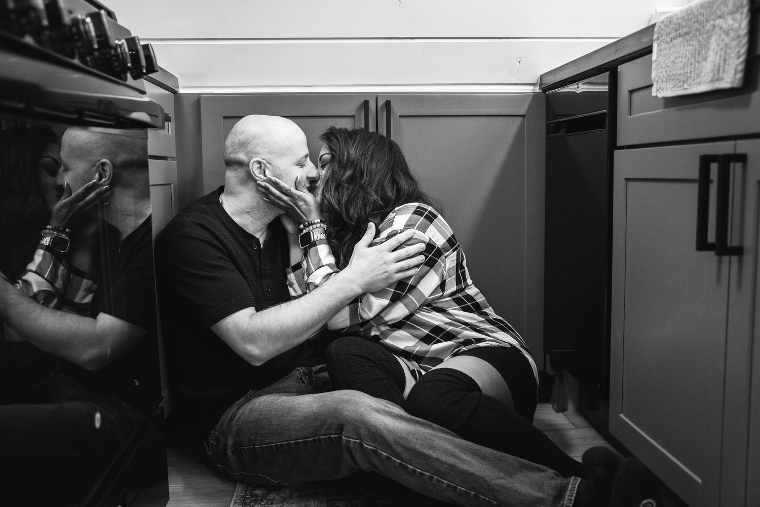 Black and white photo of couple sharing a tender kiss while sitting on a rustic cabin floor.