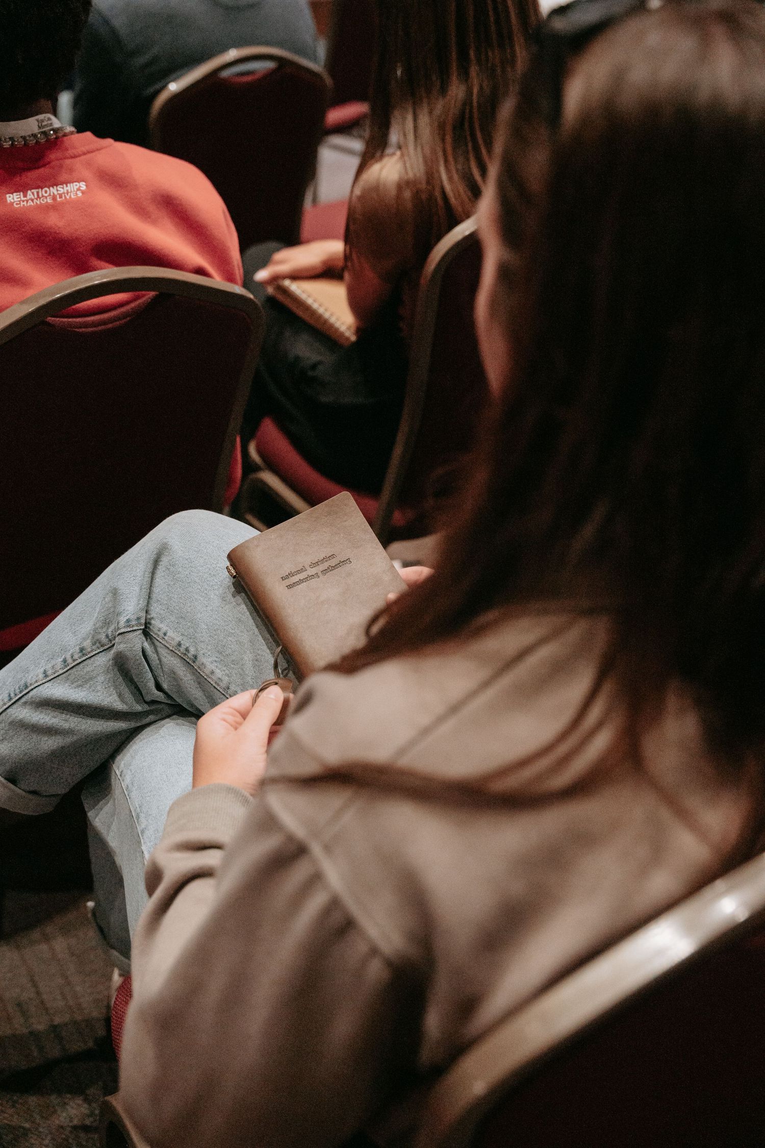Young woman sitting in auditorium chair holding a small brown book in her lap.