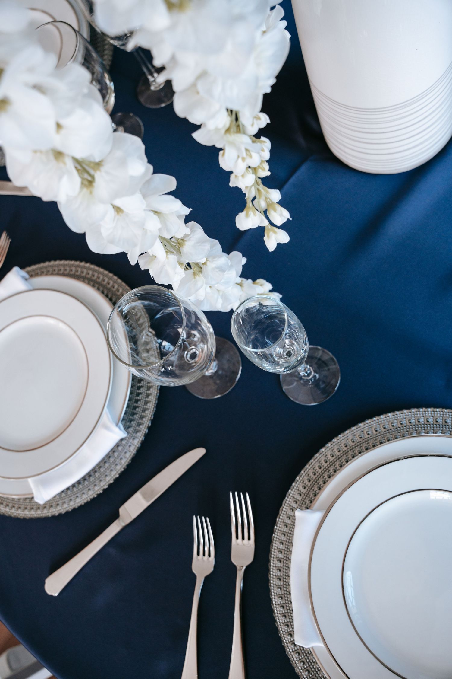 Navy blue wedding table setting with white florals, silver chargers and crystal glasses.