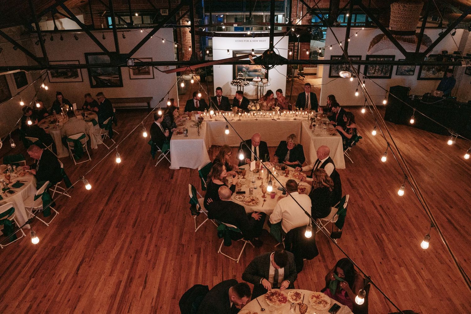 Aerial view of wedding reception with round tables, string lights, and warm candlelight in an art gallery.