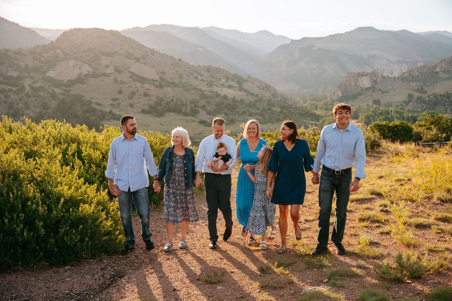 Family of six walks together through a sunlit mountain landscape during a golden hour outdoor photo session.
