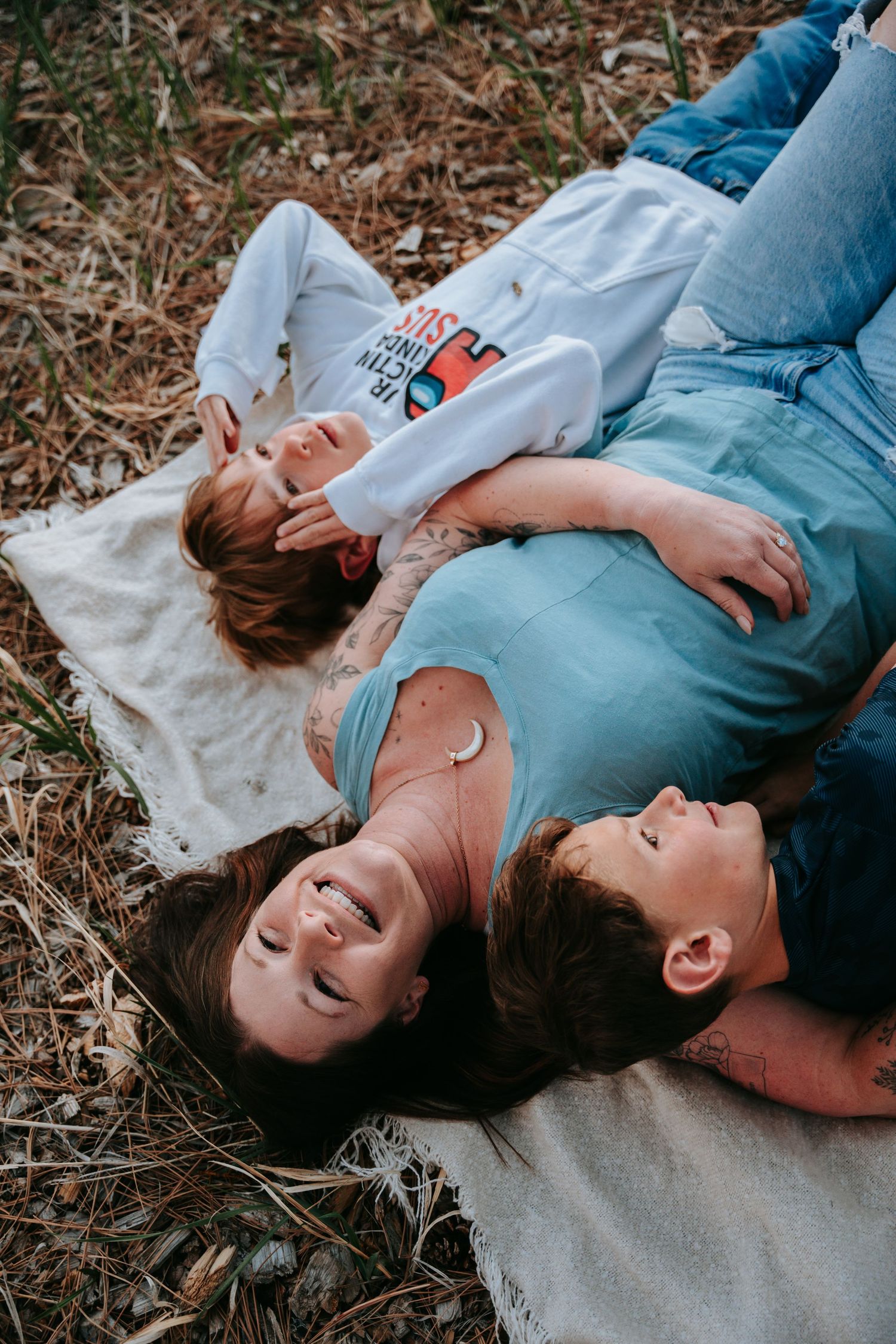 Three family members lying on a blanket outdoors smiling and relaxing together.
