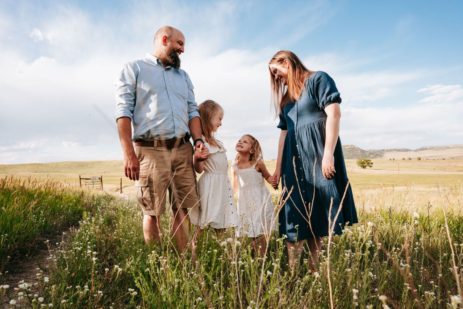 A happy family of four walking through a wildflower meadow under a bright blue sky.