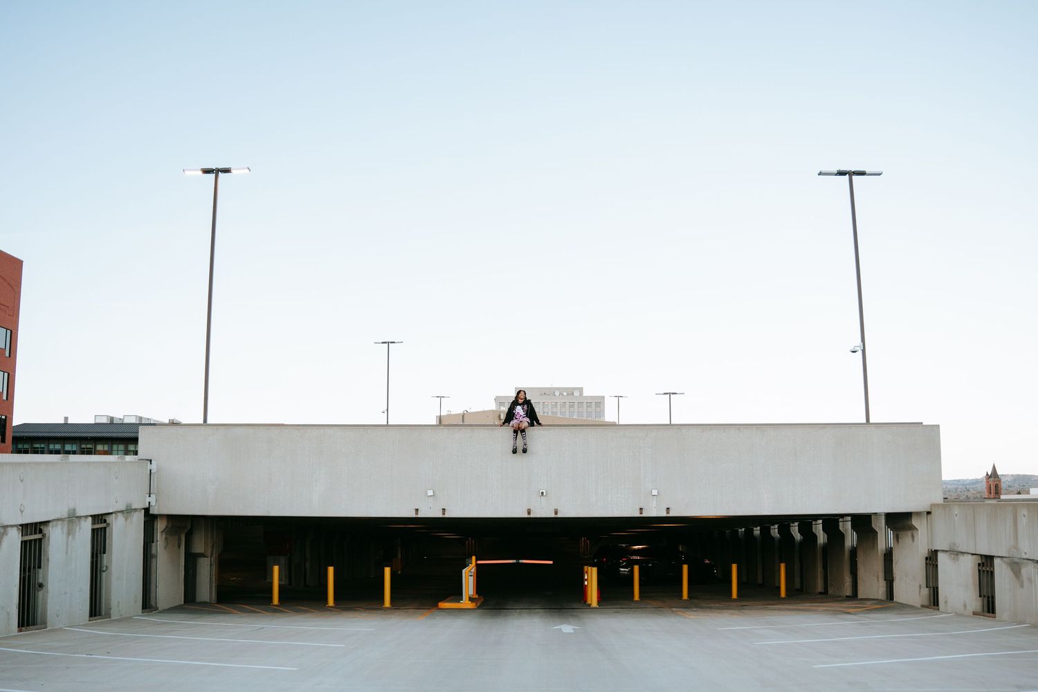 Person standing on edge of concrete parking garage rooftop against clear blue sky.