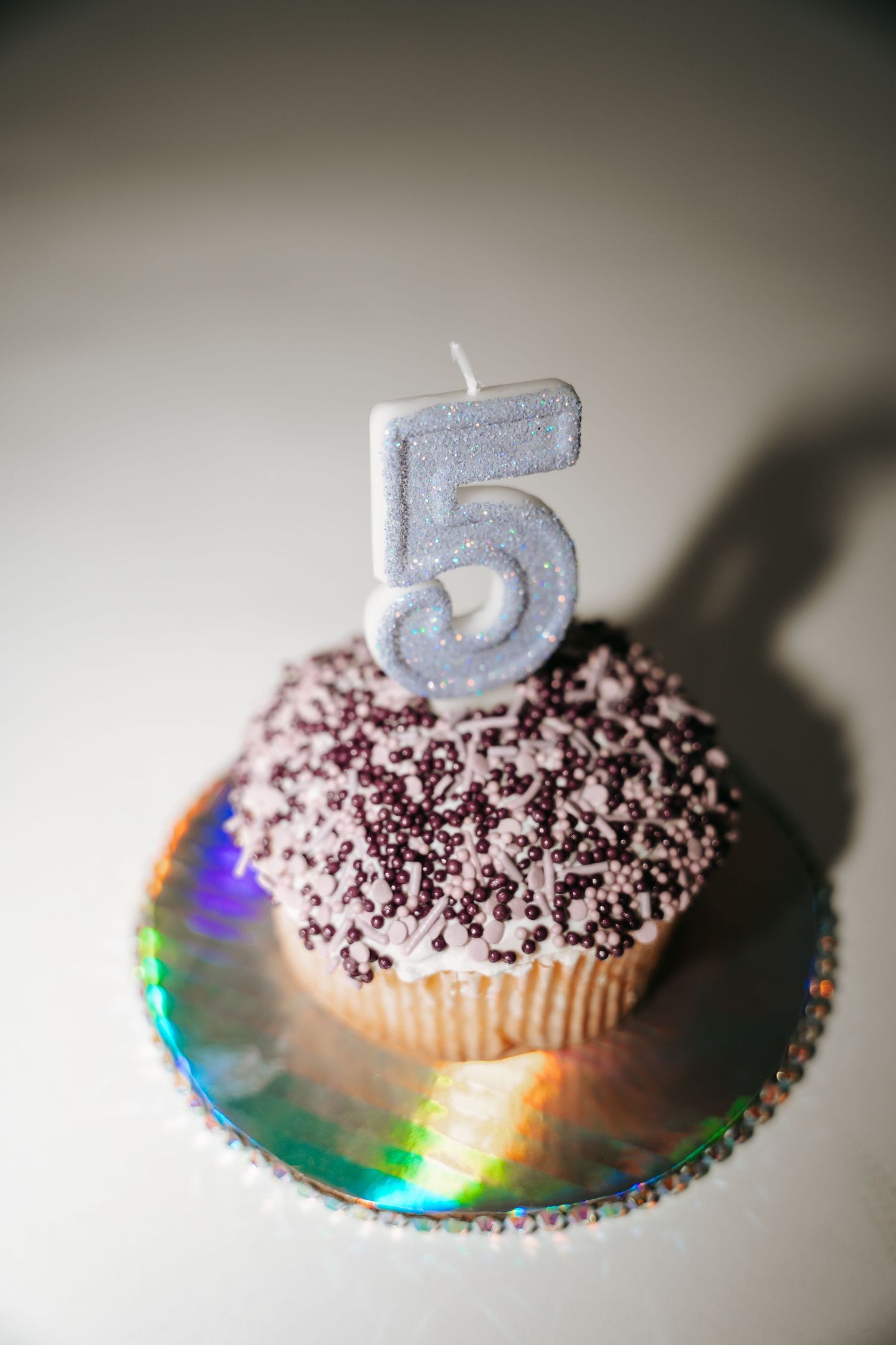 Close-up of a purple sprinkle cupcake with a glittery number five candle on a holographic iridescent plate.