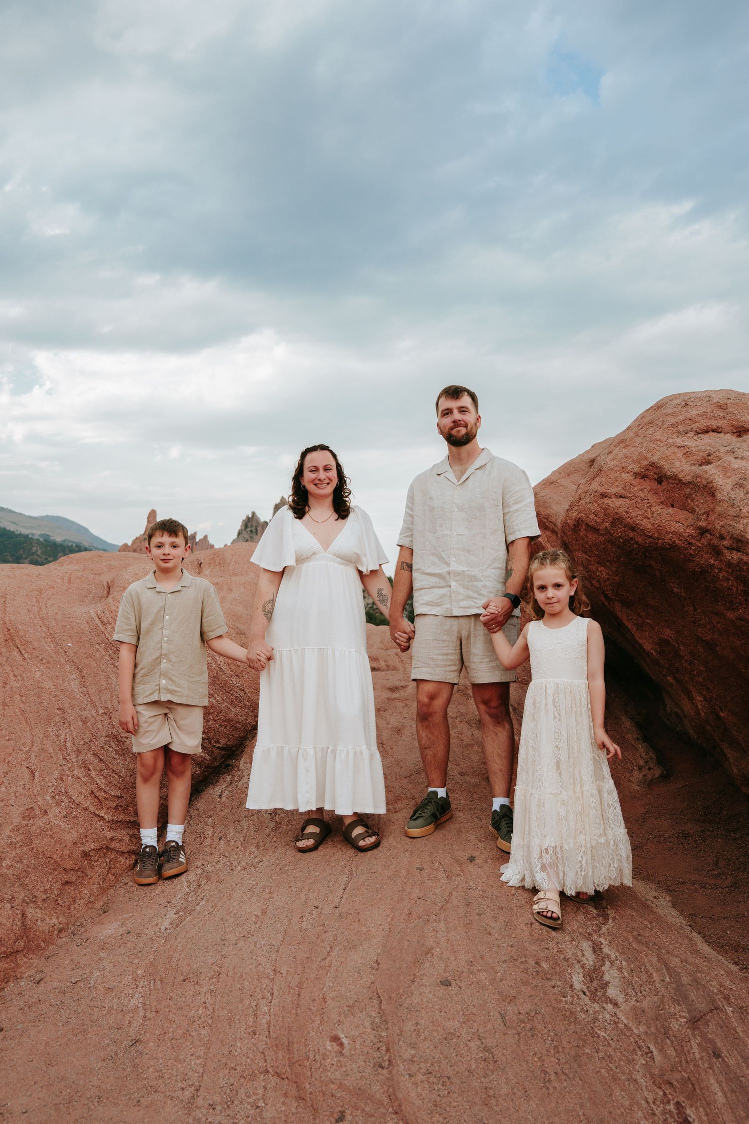 Family of four poses among red rock formations at Garden of the Gods, Colorado, wearing coordinated neutral and white outfits.