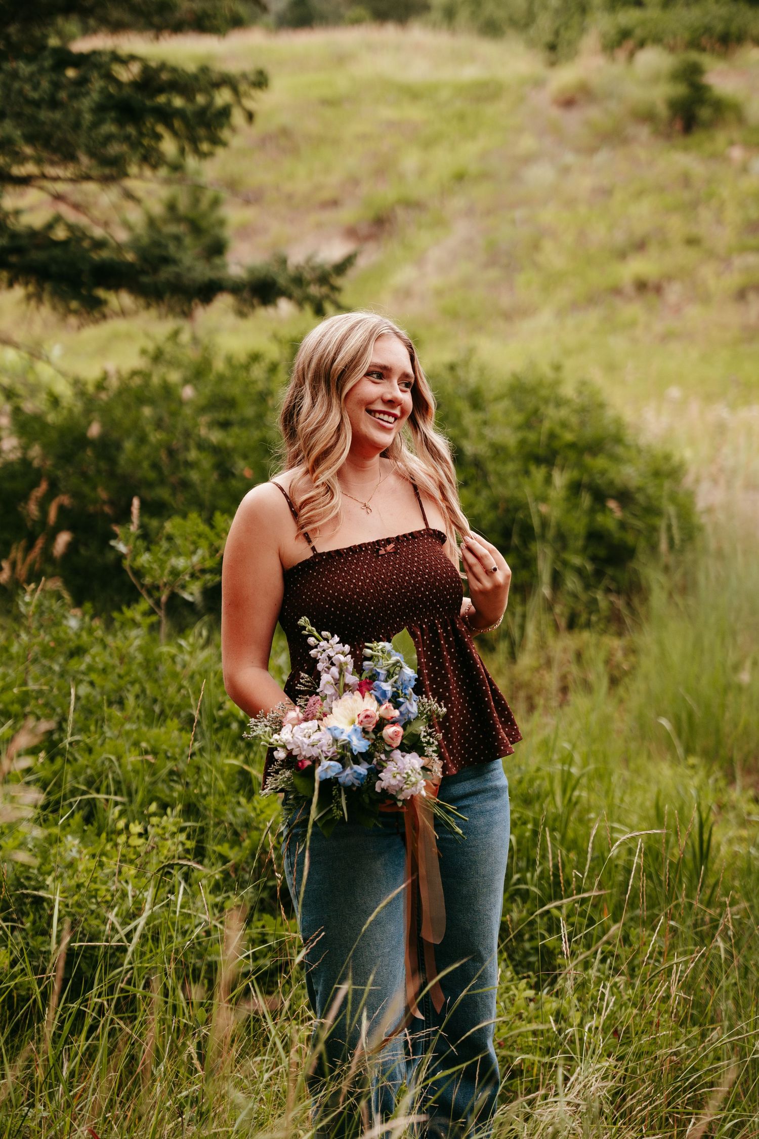 Blonde woman in a brown polka dot top holding a colorful flower bouquet in a green field.
