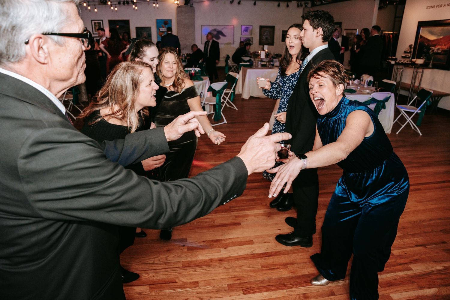 Energetic wedding guests dance and reach toward each other on the reception dance floor.