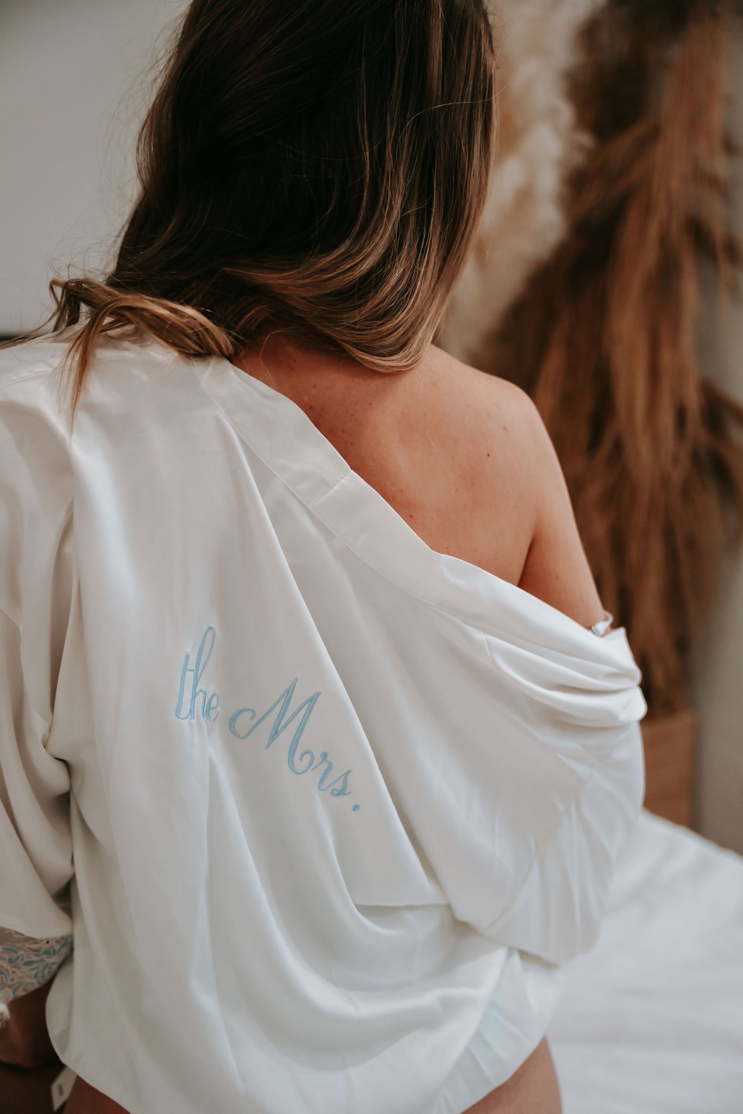 Bride wearing white satin robe with The Mrs. script on back in elegant bridal boudoir photo.