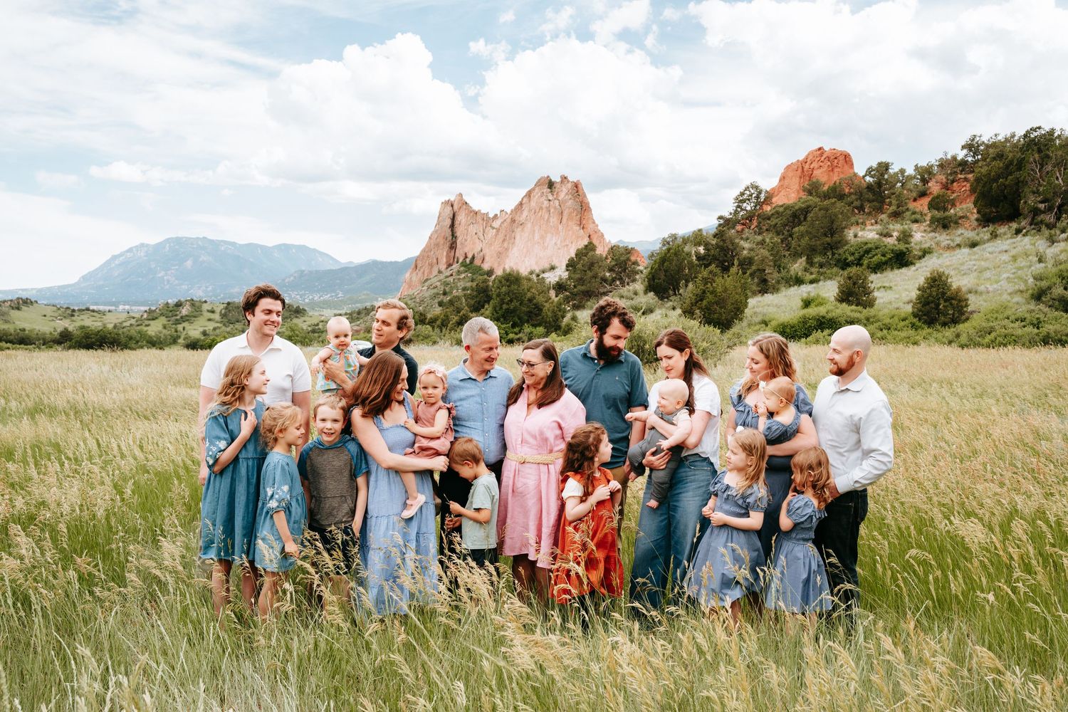 Large extended family gathers in a tall grass field with Garden of the Gods rock formations in background.