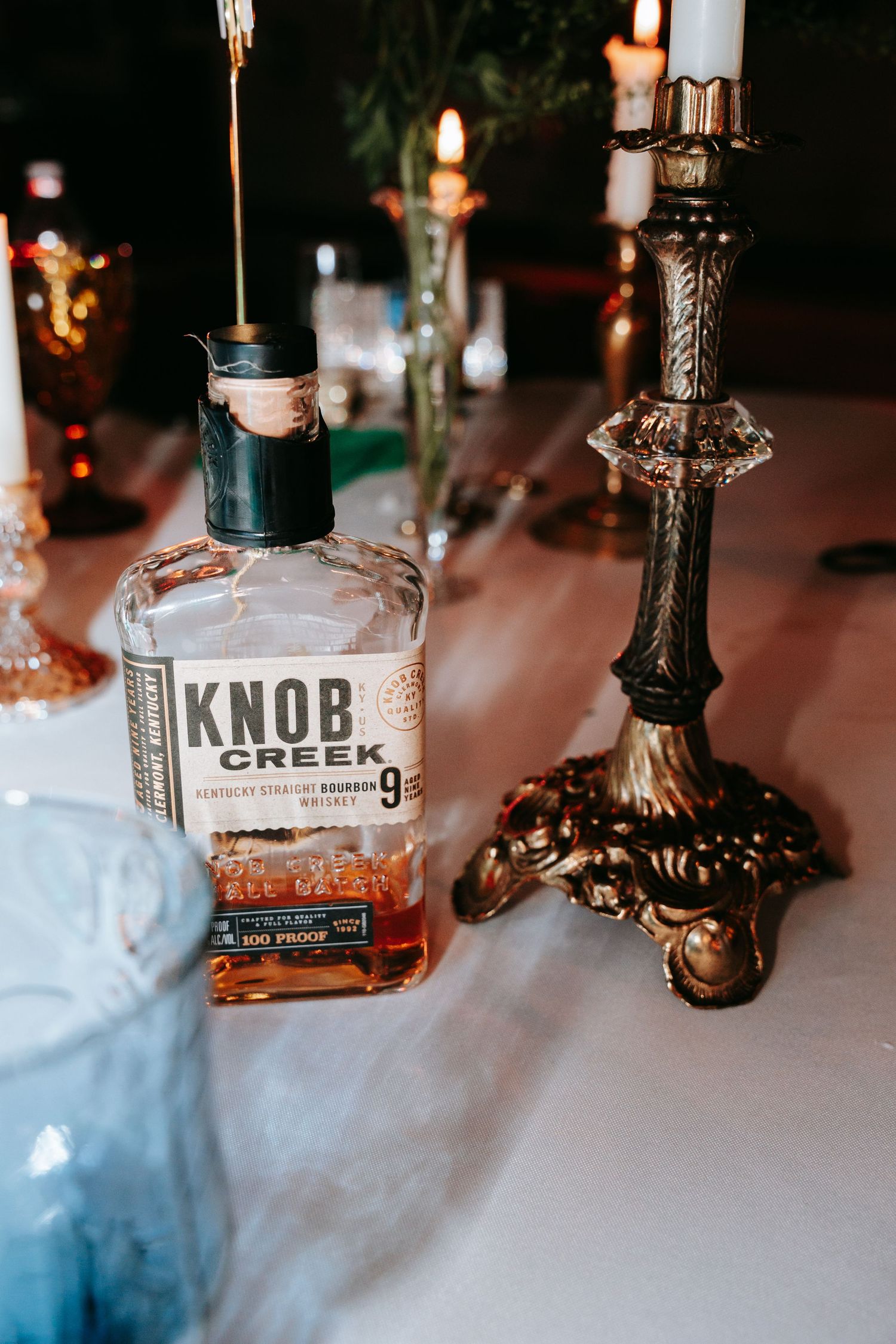 Knob Creek bourbon whiskey bottle beside an ornate brass candlestick at a wedding.
