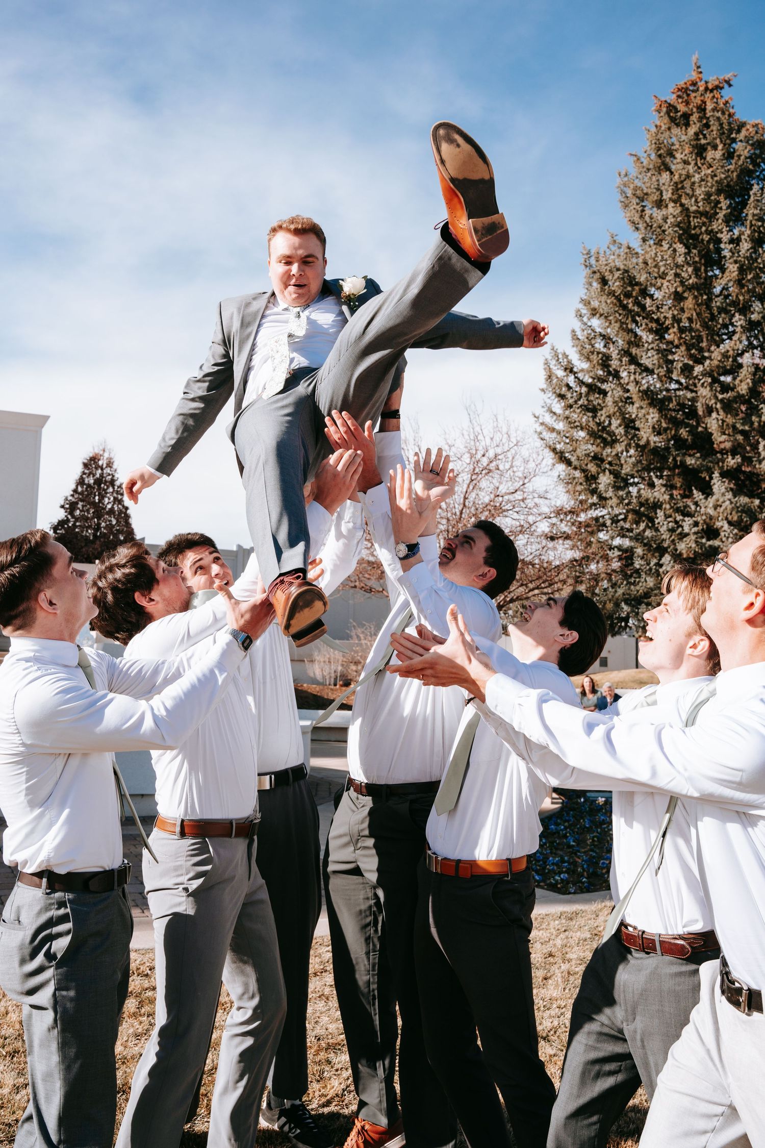 Groomsmen tossing groom into the air outdoors on a sunny winter wedding day.
