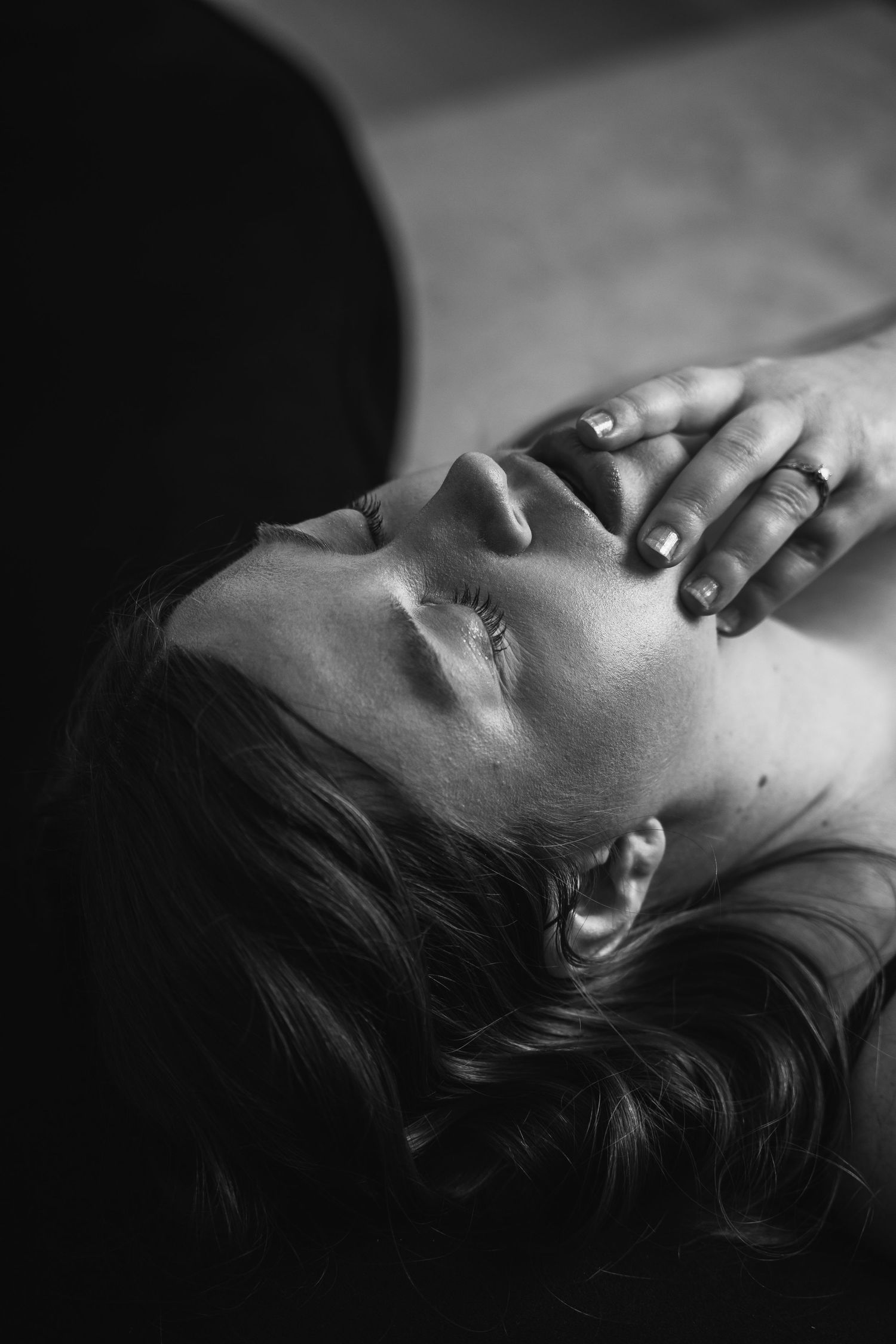 Black and white photo of a woman lying down with eyes closed, hand gently placed on her face.