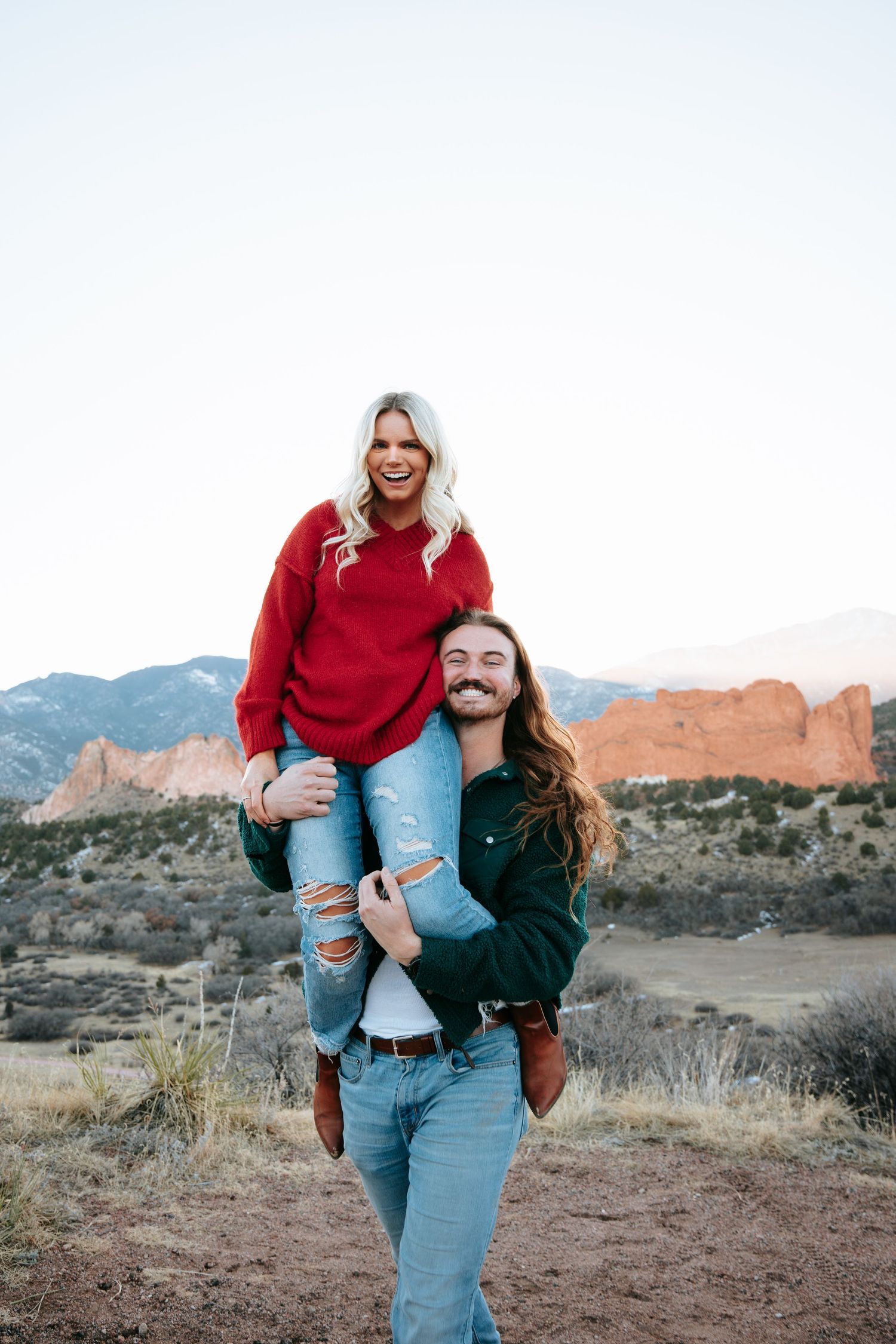 A laughing woman in a red sweater being carried on a mans shoulders at Garden of the Gods.
