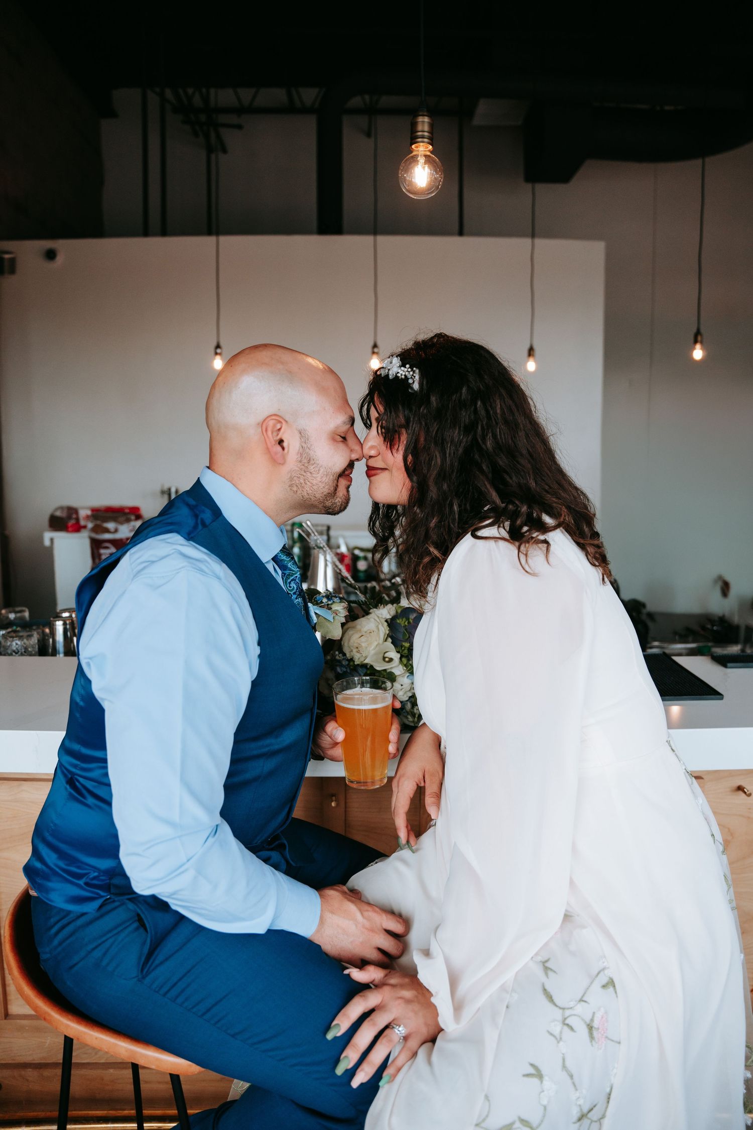 Bride and groom sharing a kiss at a bar with warm Edison bulb lighting at wedding.