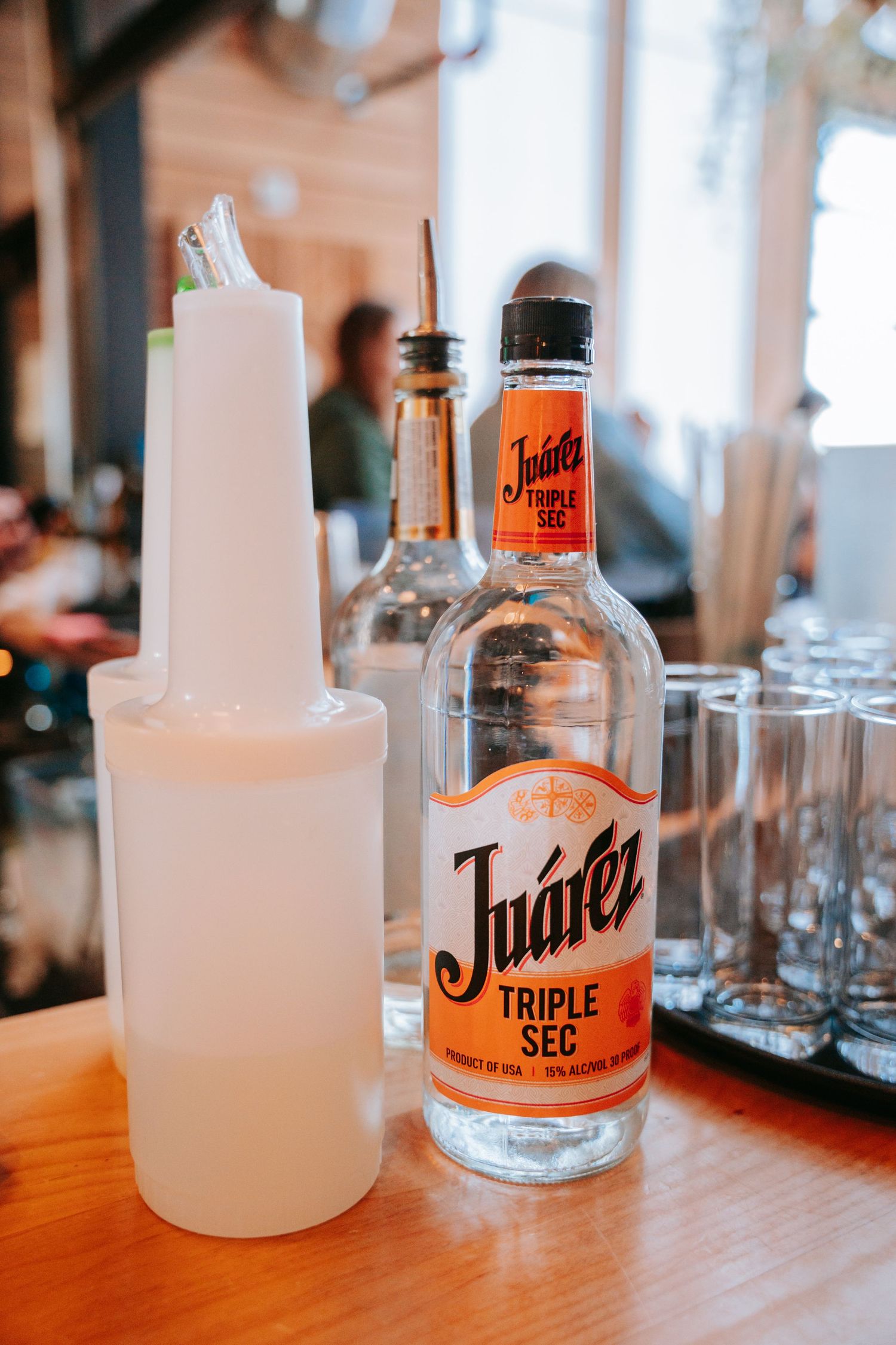 Bottle of Juarez Triple Sec liqueur on a wooden bar counter with glassware in background.