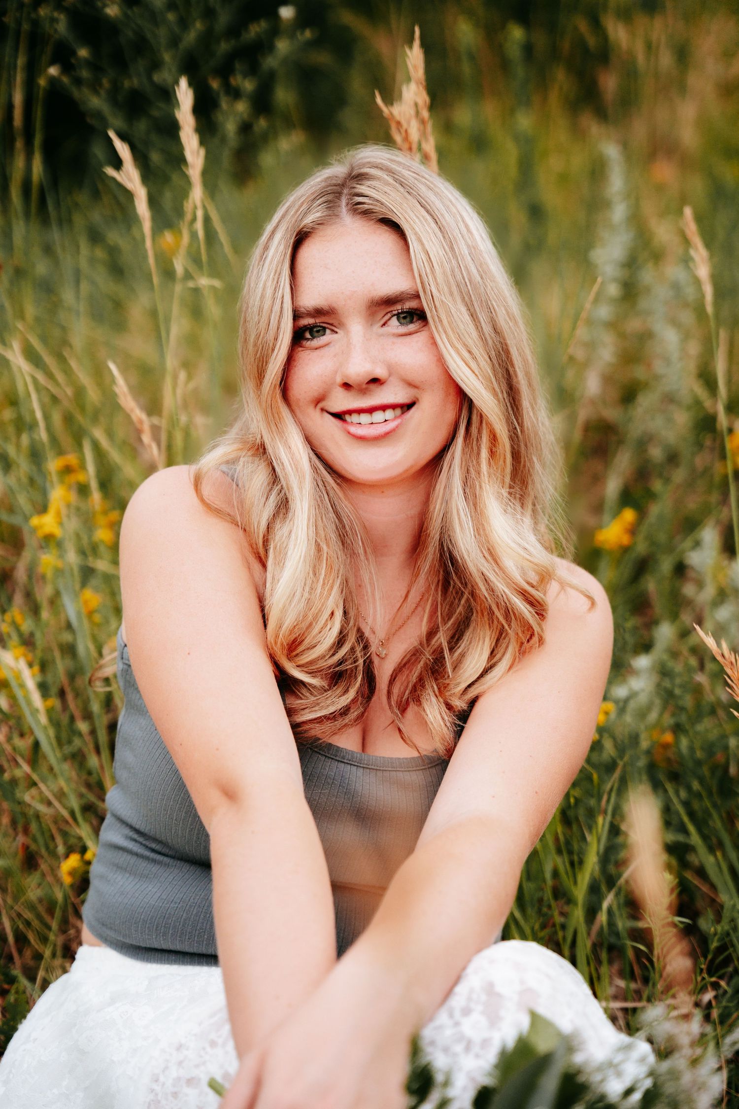 Close-up portrait of a smiling blonde woman sitting in a field of tall golden grass.