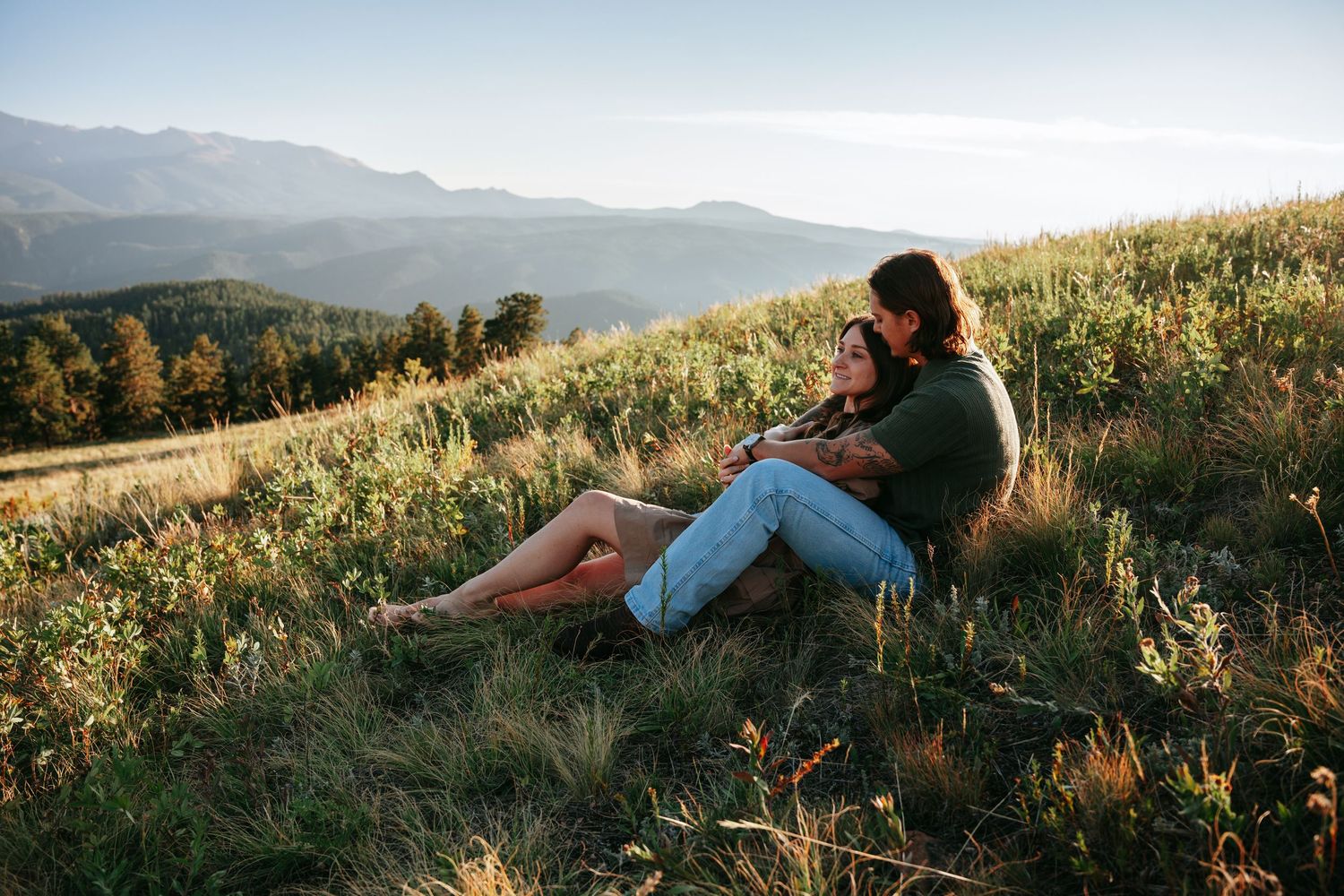 Couple sitting together on a mountain hillside at golden hour with scenic valley views.