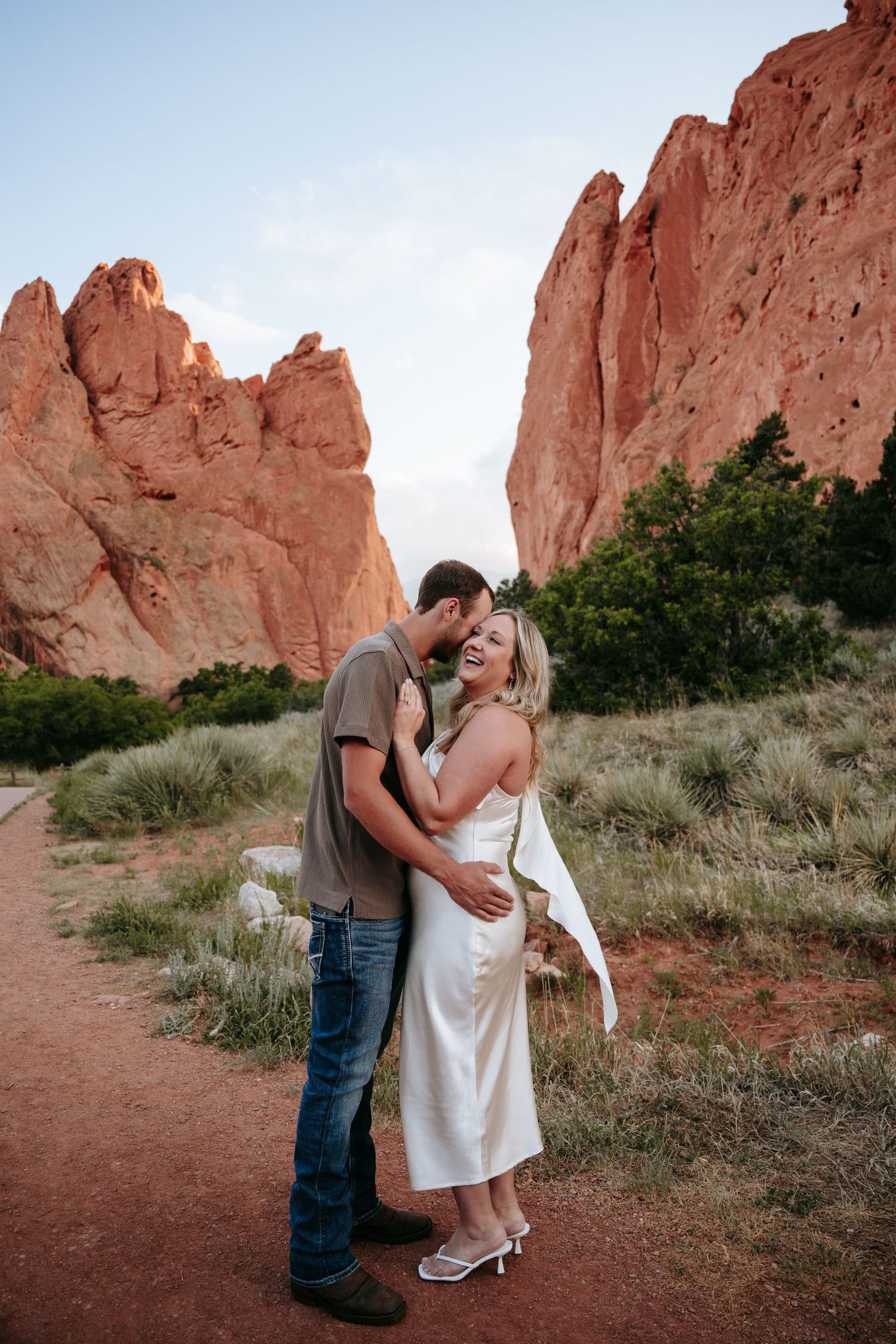 Couple embracing and laughing at Garden of the Gods, Colorado, with red rock formations in the background.