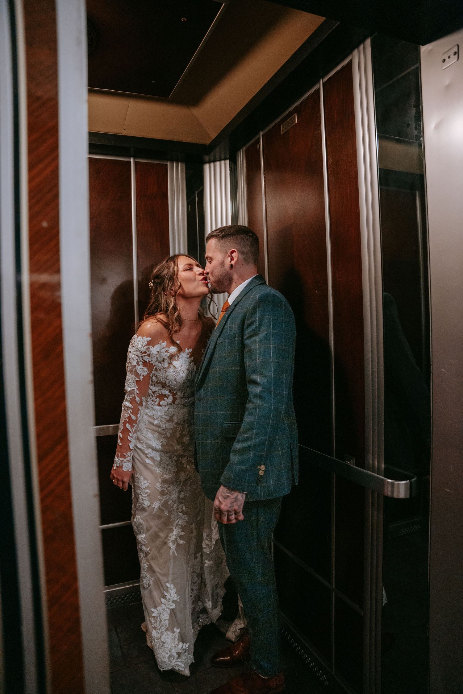 Bride and groom share an intimate kiss inside a wood-paneled elevator on their wedding day.