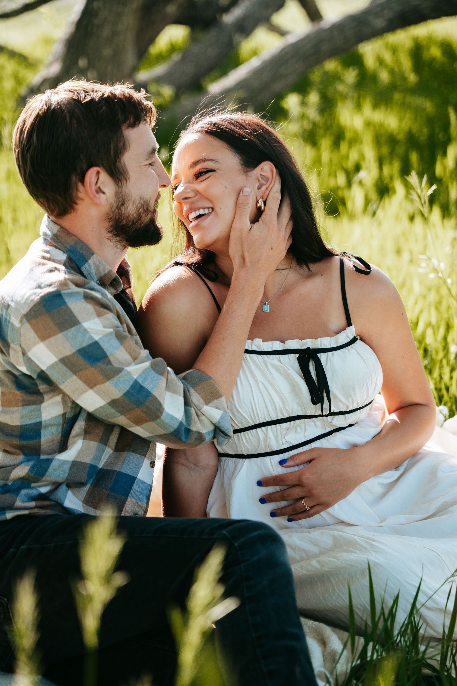Happy pregnant couple sharing romantic moment sitting together in lush green outdoor setting.