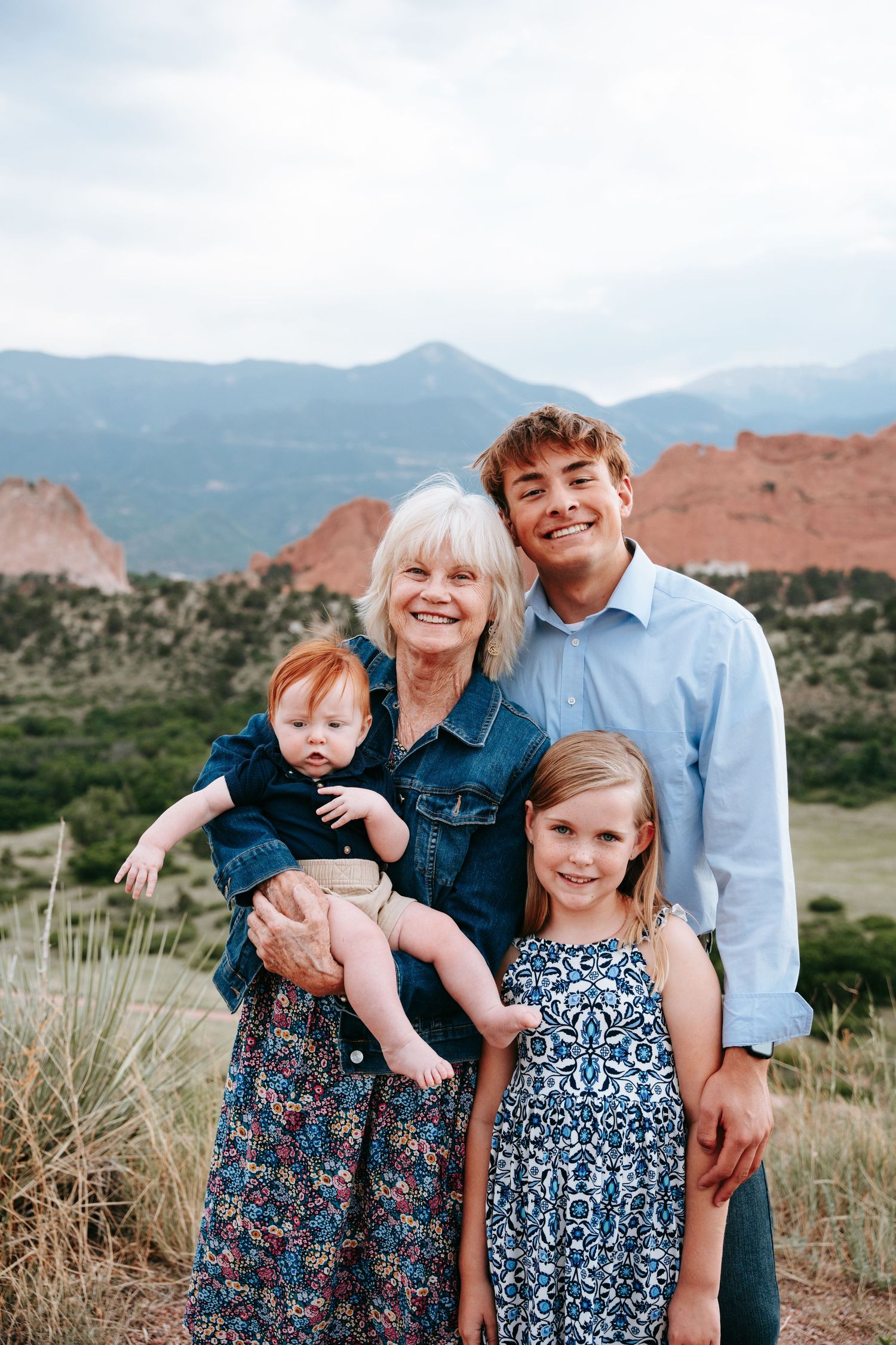 Grandmother with teenage boy and young girl holding baby outdoors with red rock formations.