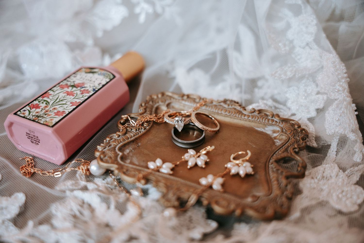Wedding day details with gold rings, pearl earrings, perfume bottle, and jewelry on ornate tray.