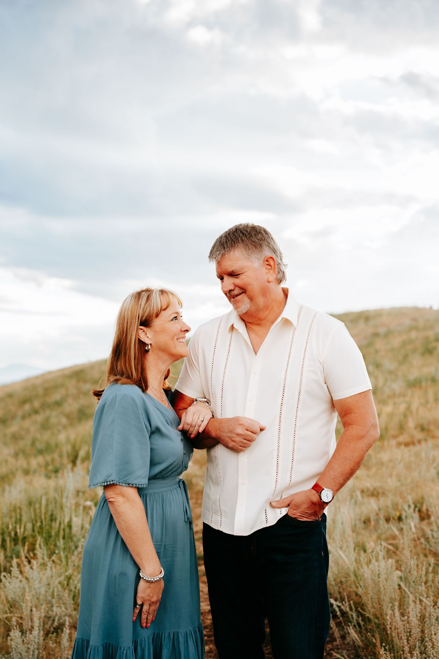 Smiling mature couple holding hands and laughing together in a wide open grassy field outdoors.