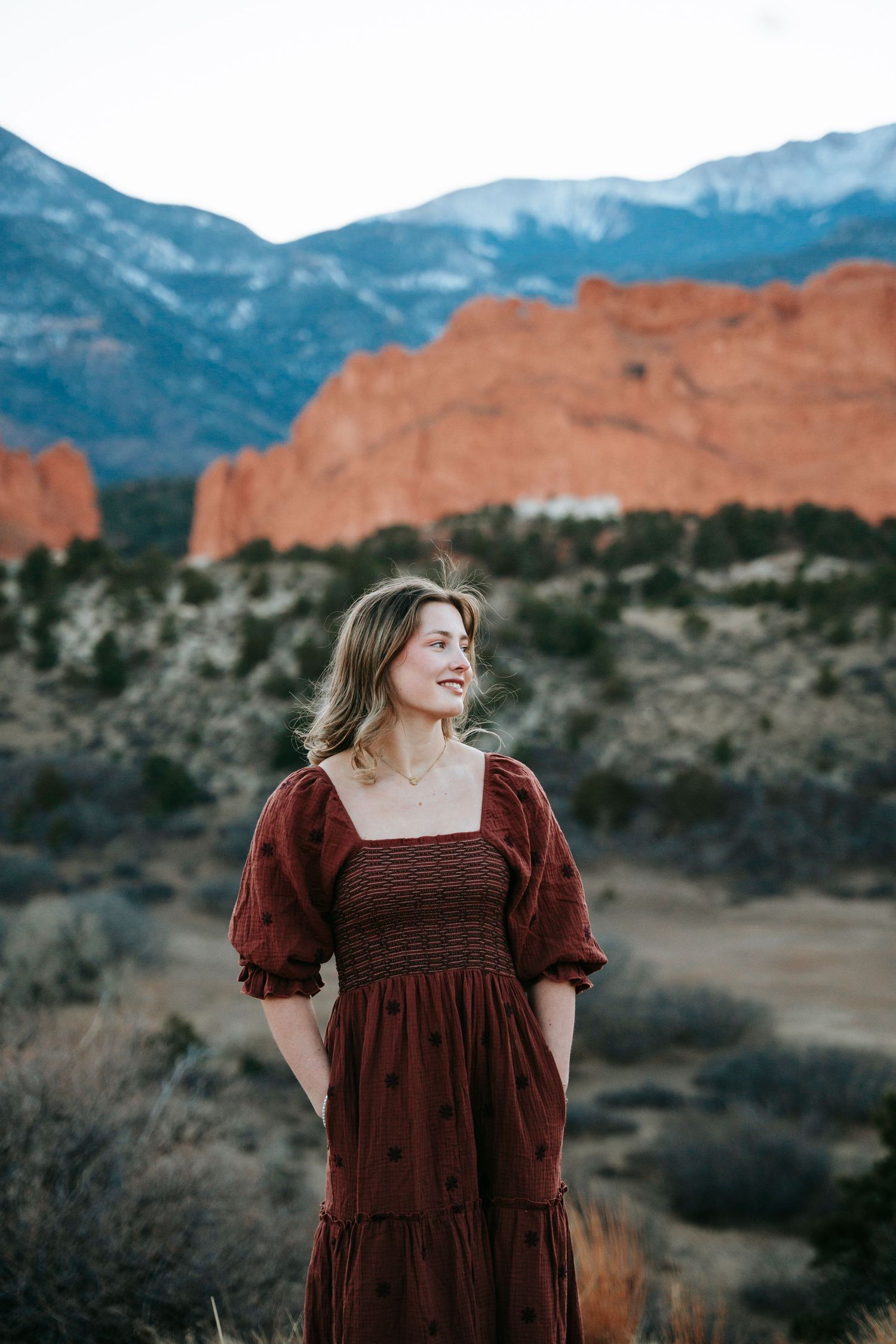 Young woman in red smocked dress standing at Garden of the Gods with mountain views.