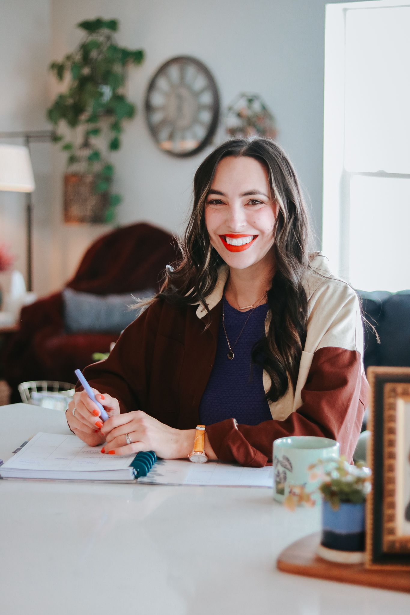 Smiling brunette woman with red lips writing in notebook at white desk in cozy home office.