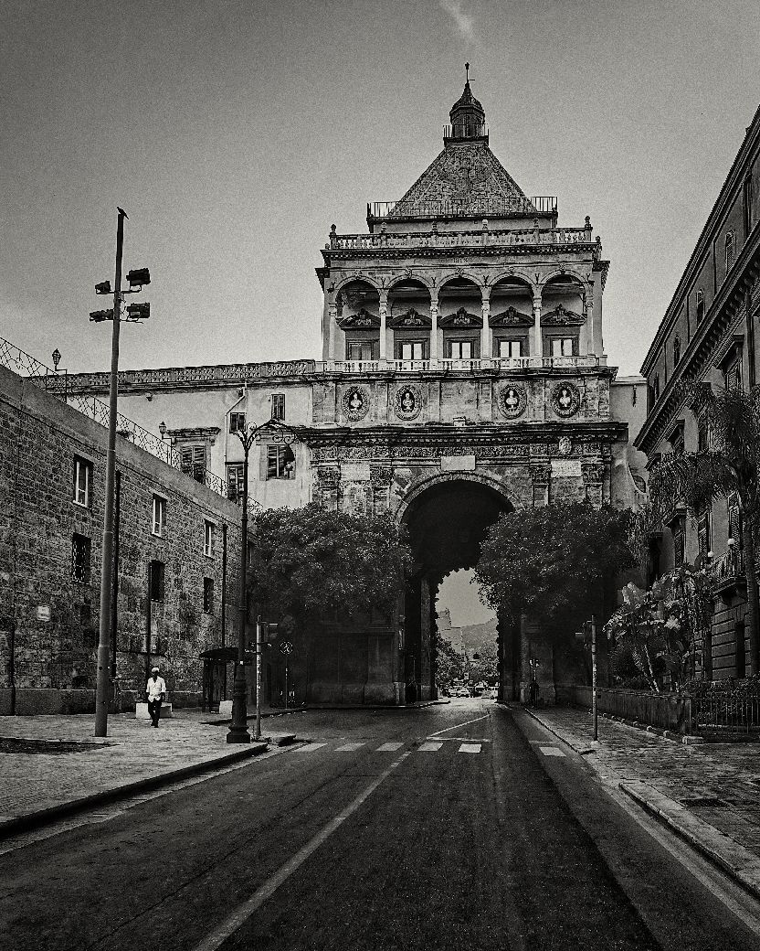 Black and white panoramic view of a historic building with ornate architecture along an empty street.