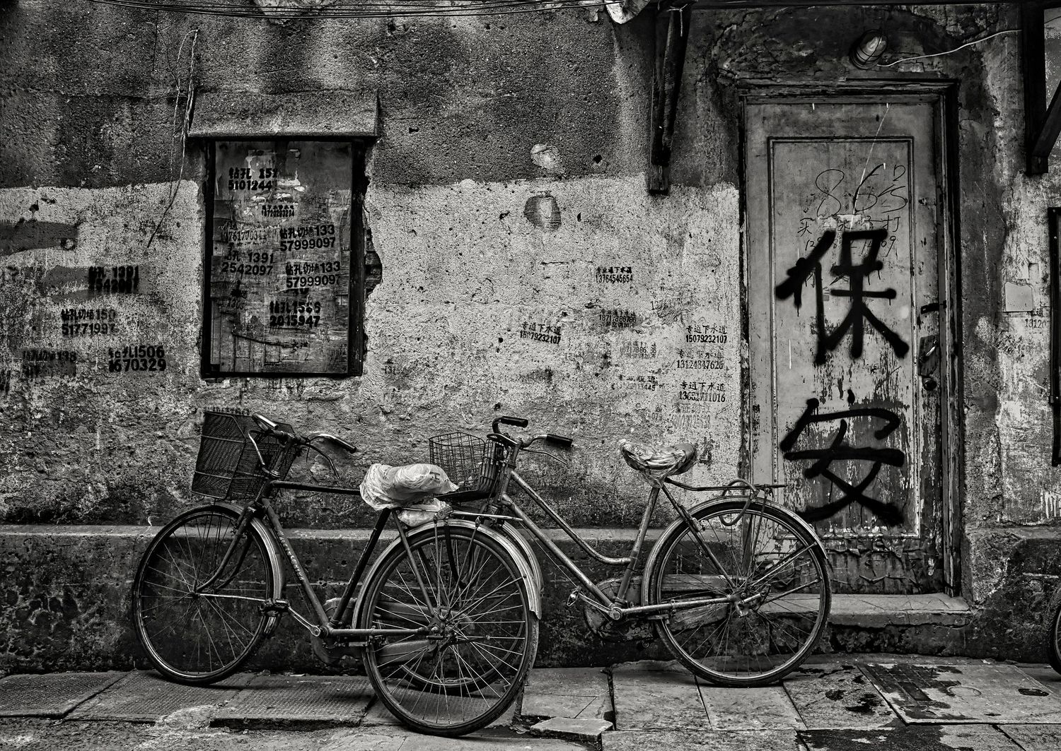 A row of vintage bicycles parked against weathered stone walls with graffiti in black and white tones.