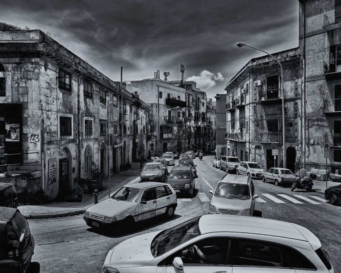 Dramatic black and white panoramic cityscape showing parked cars along narrow streets with moody storm clouds overhead.
Horvath-Photography-