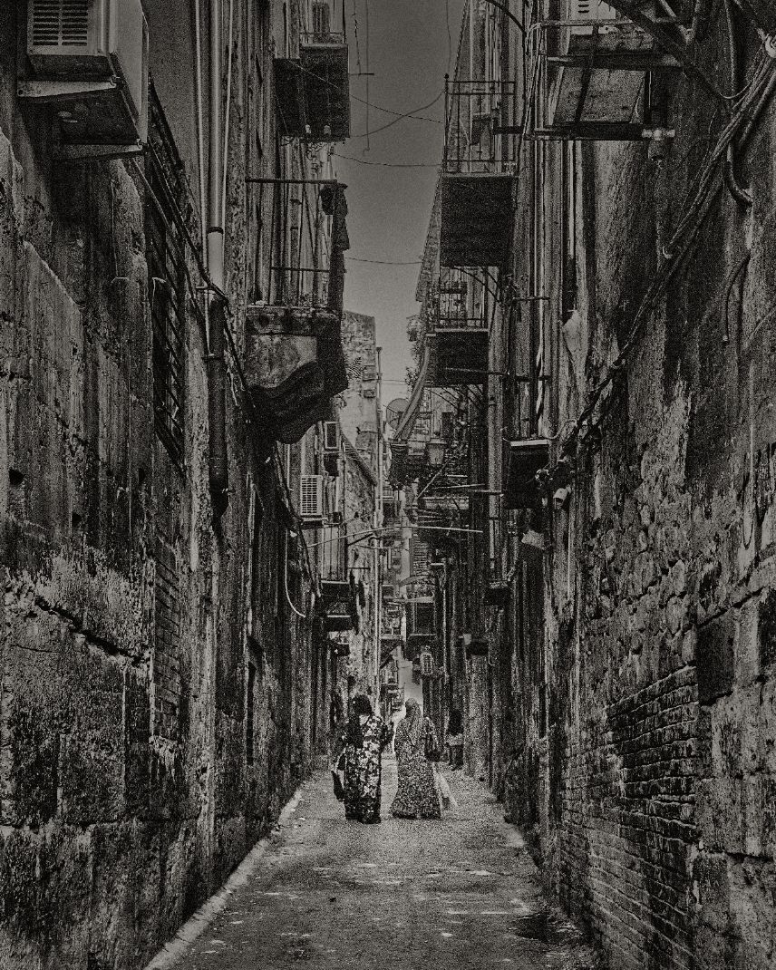 A black and white urban alley in Hong Kong with tall buildings and laundry lines stretching between them.