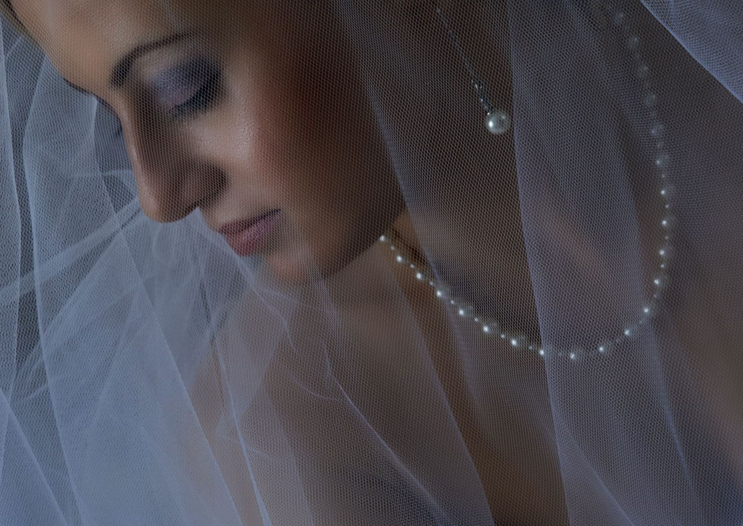 A bride in a white veil and wedding dress gazes downward with a serene expression during her wedding preparations.