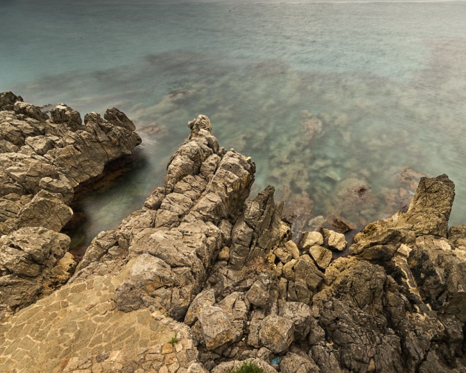 Rocky coastal shoreline with rugged limestone formations against turquoise Mediterranean waters.